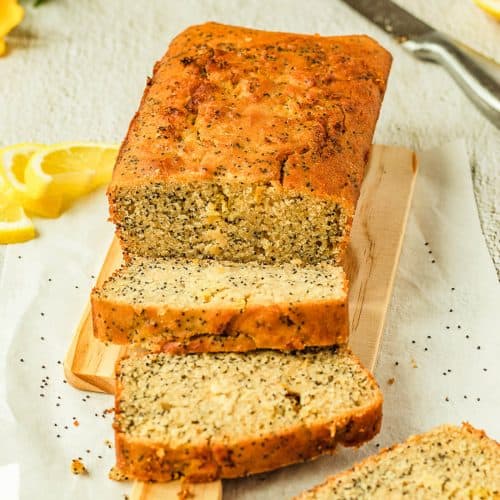 A Sliced Lemon Poppy Seed Loaf on a Bread Board, there are some lemon slices as a decoration to the side.