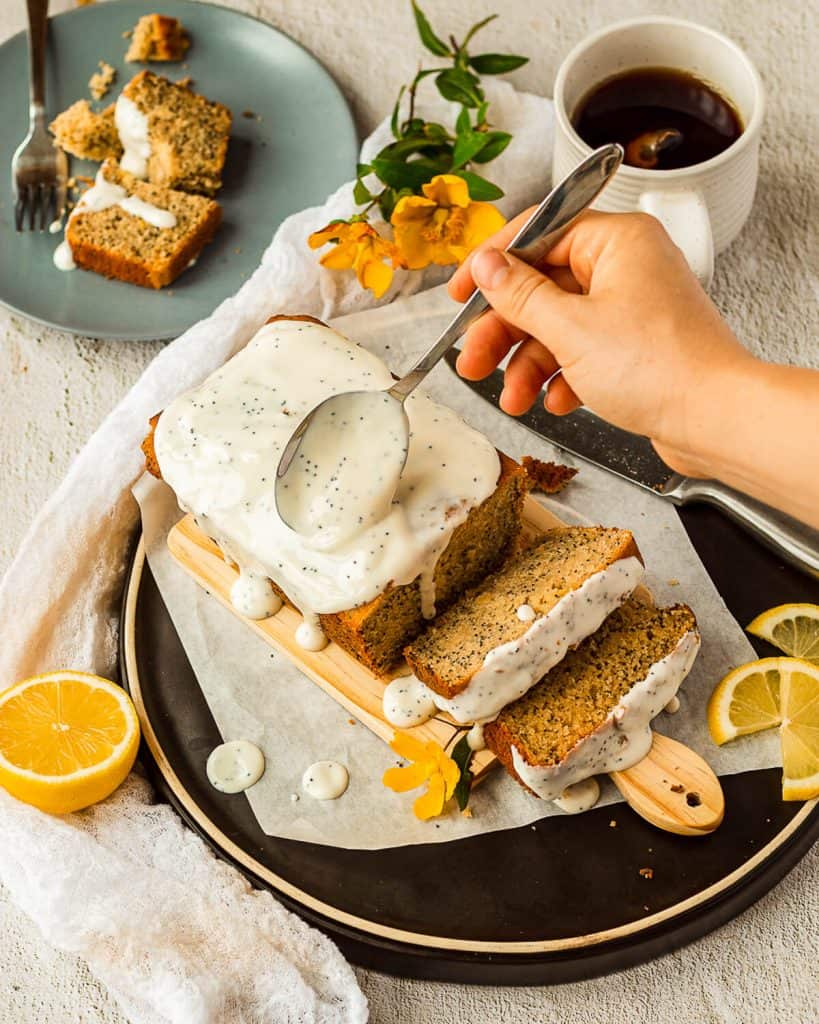 Someone is spooning some yoghurt onto a lemon poppy seed loaf.