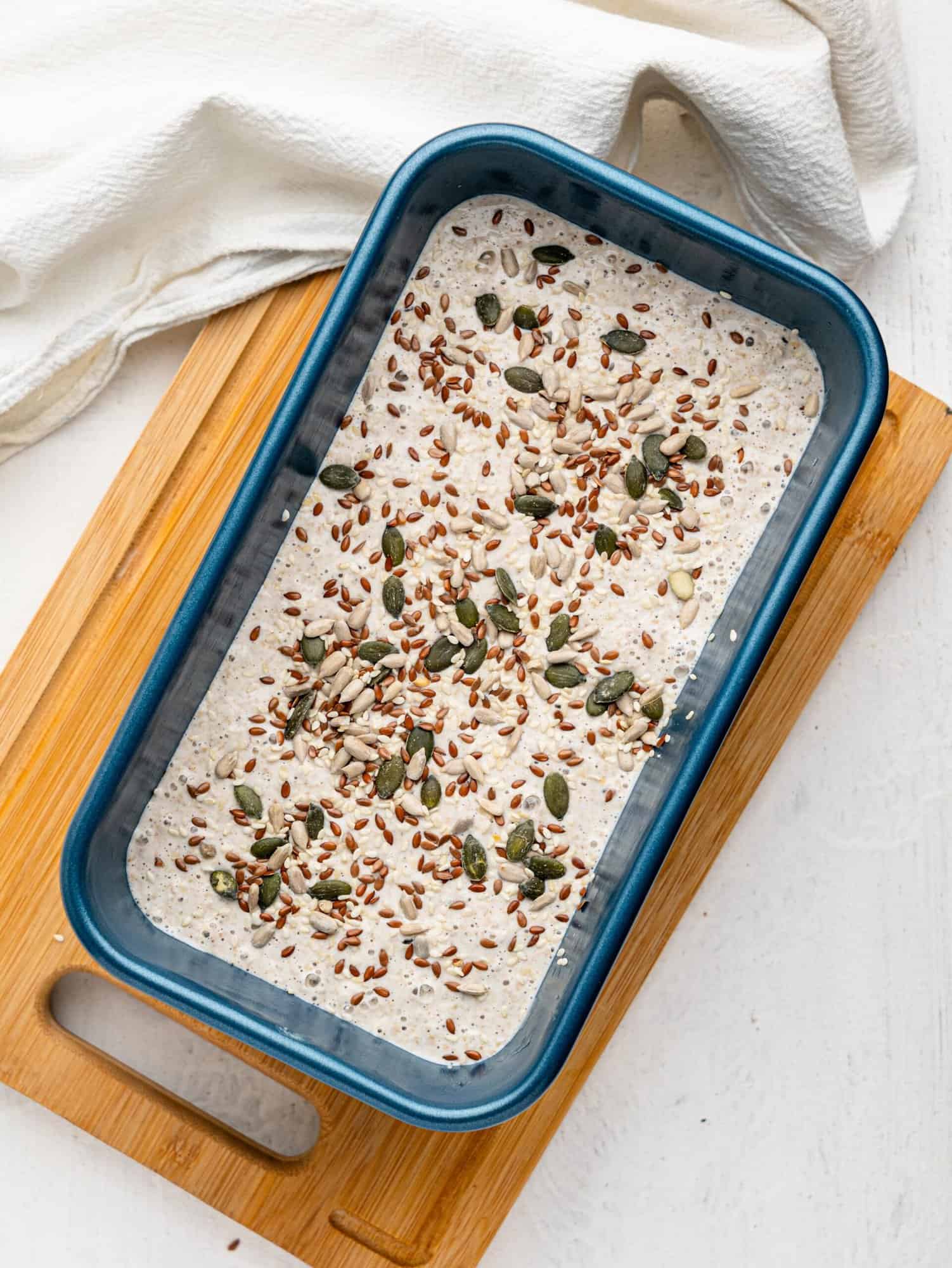 Buckwheat bread mixture with seeds on top in a loaf pan