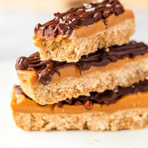 Three vegan millionaires shortbread bars stacked on top of each other, a bite has been taken from the top one.