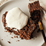 A slice of healthy chocolate loaf cake on a plate with some vegan yoghurt on top. There is a fork to the side with a bit of cake on.
