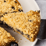 a slice of blueberry crumb cake is being taken with a cake slicer