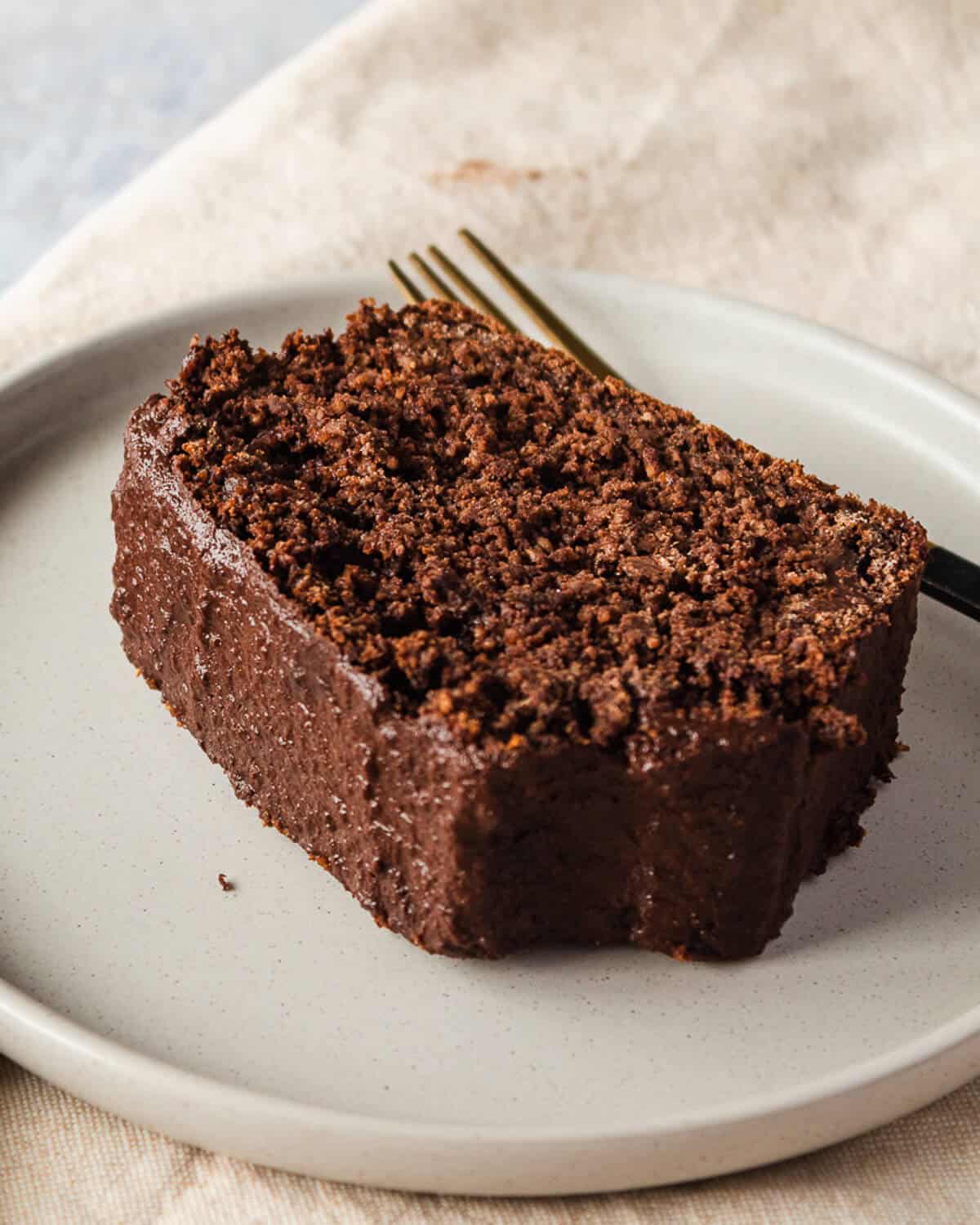 a slice of chocolate loaf cake on a grey plate with a fork behind it.