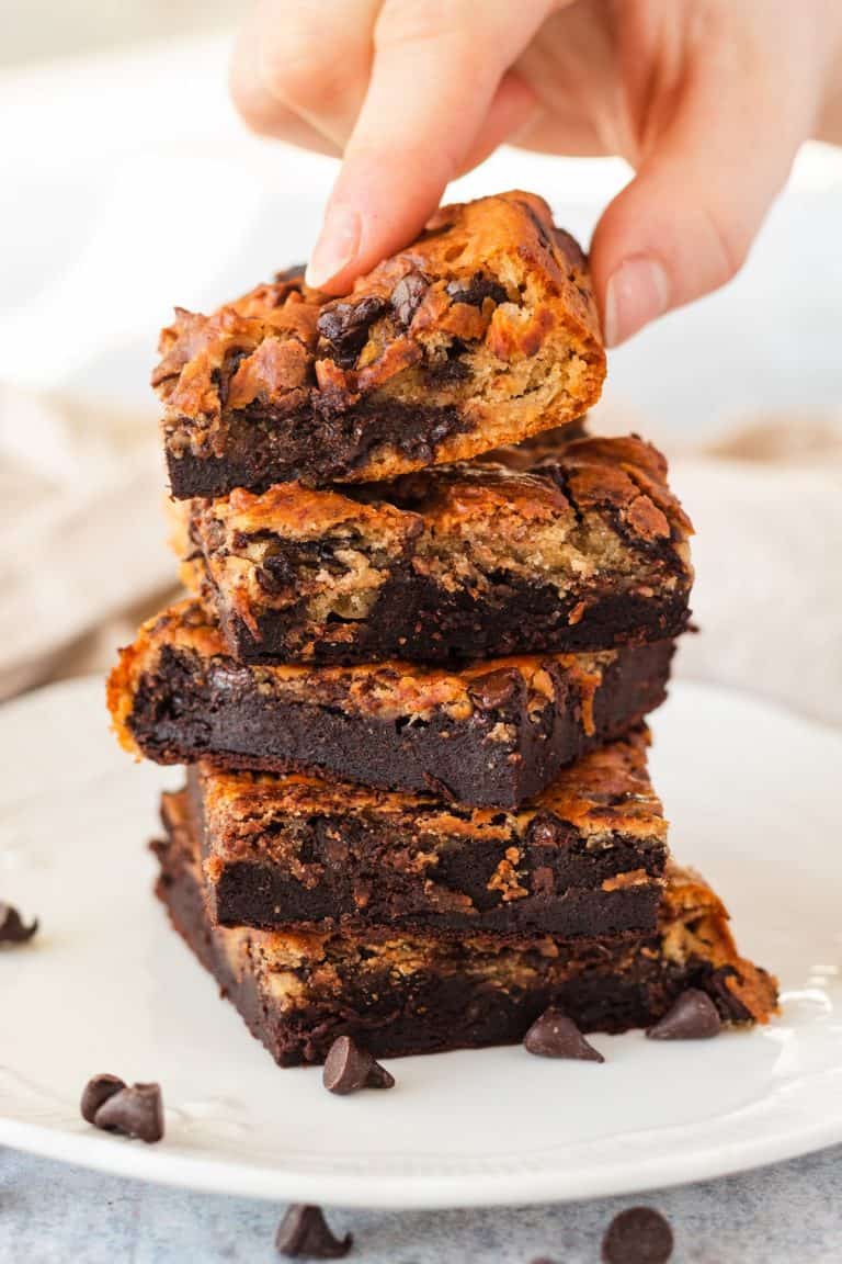 A stack of five healthy vegan blondie brownies on a plate, a hand is holding the top one