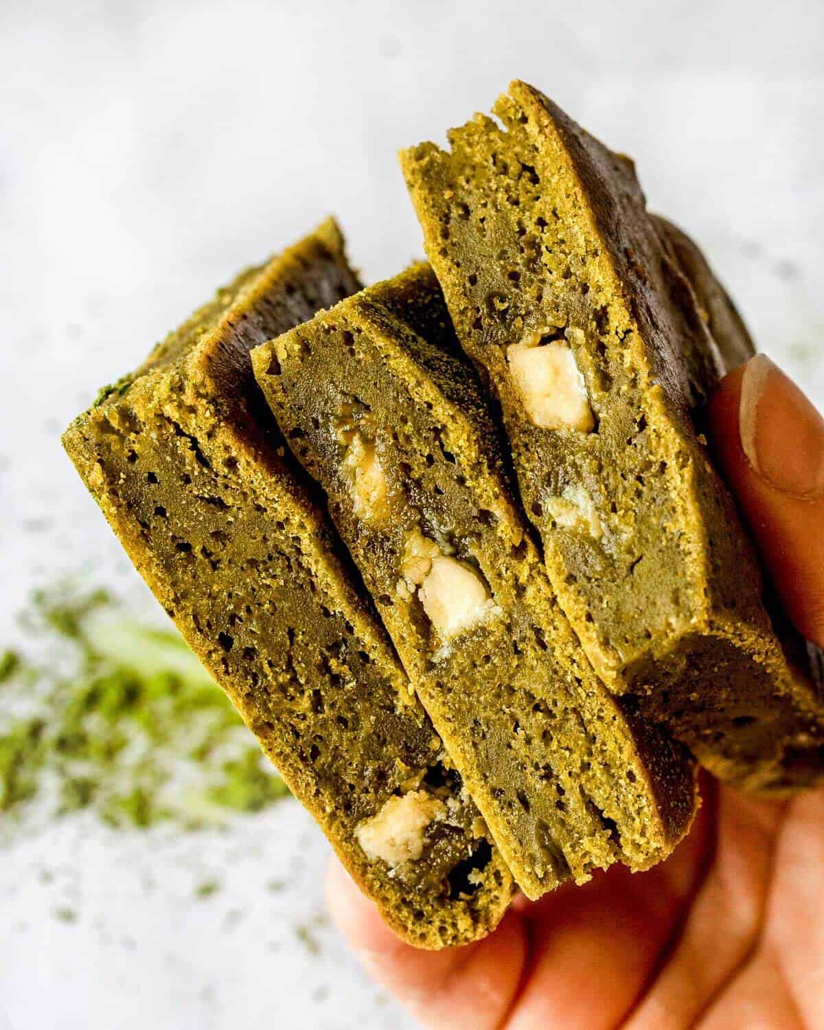 A hand holding three matcha brownies.