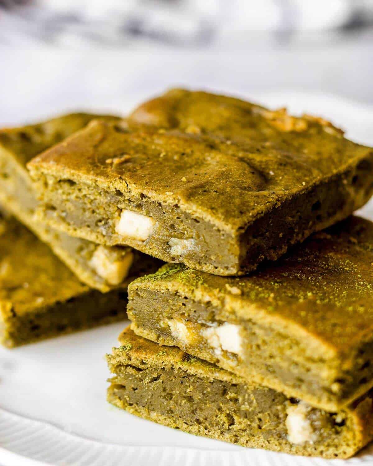 Five matcha brownies with white chocolate stacked on a white plate.