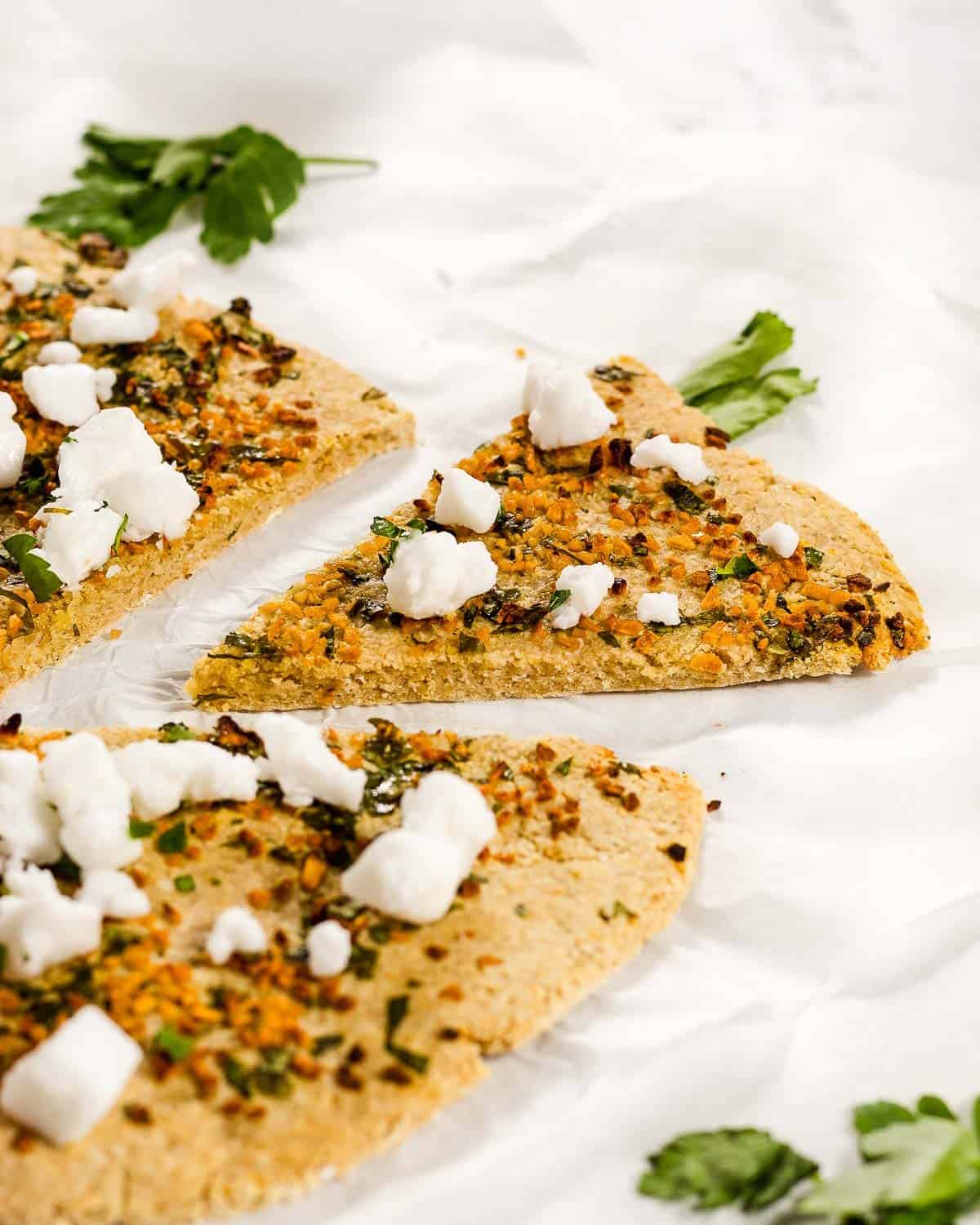 Pizza with garlic, parsley and feta. A slice has been cut and is pulled away from the rest of the pizza.