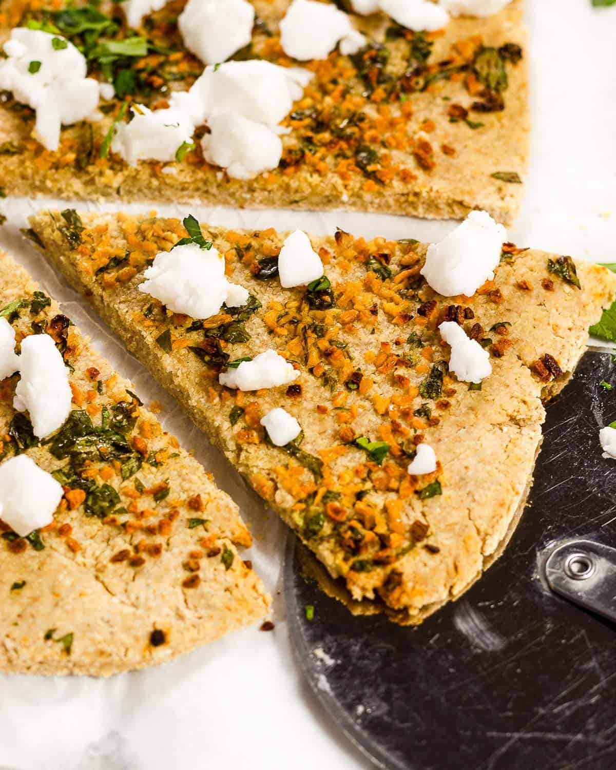 3 ingredient oat flour Pizza with garlic, parsley and feta. A slice has been cut and is positioned on a pizza wheel