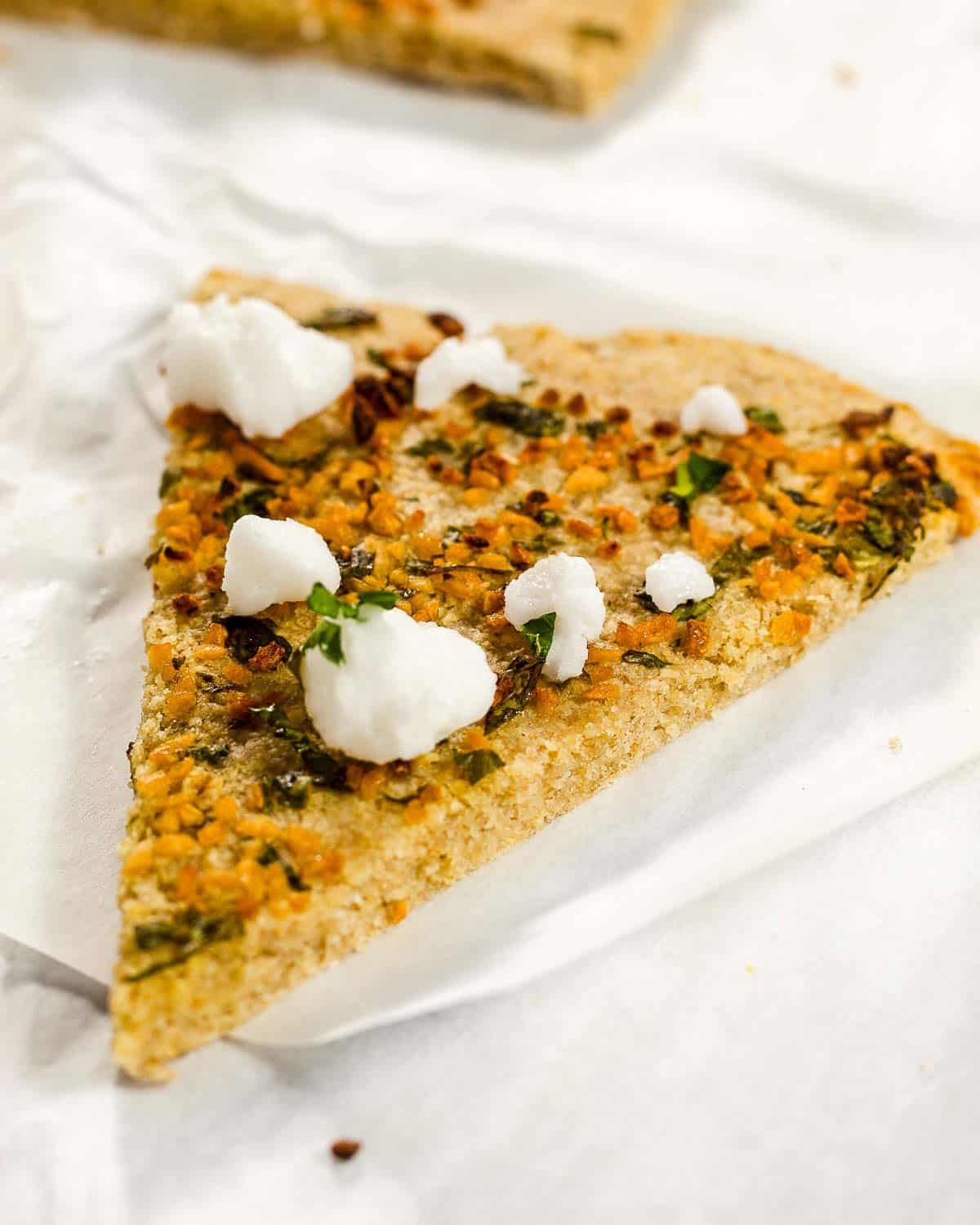 A slice of oat flour pizza with garlic, parsley and feta.