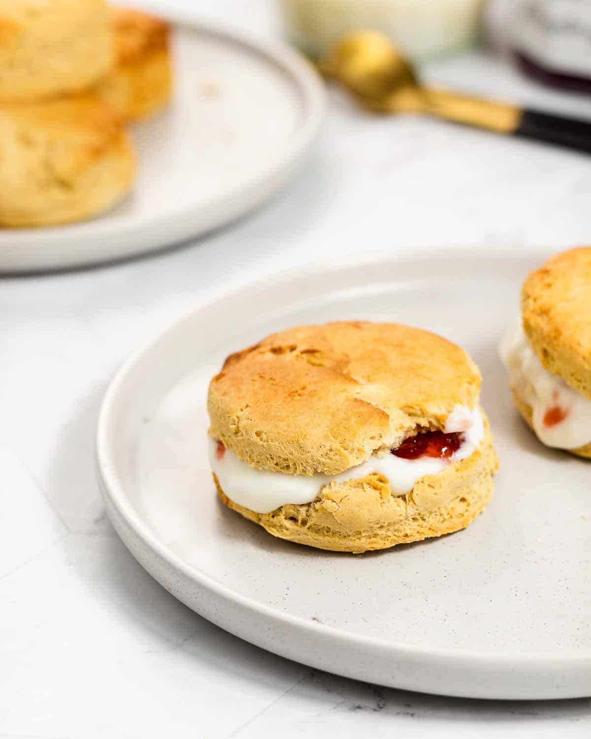 Two scones with yoghurt and jam on a grey plate. In the background there is a plate with some more scones.