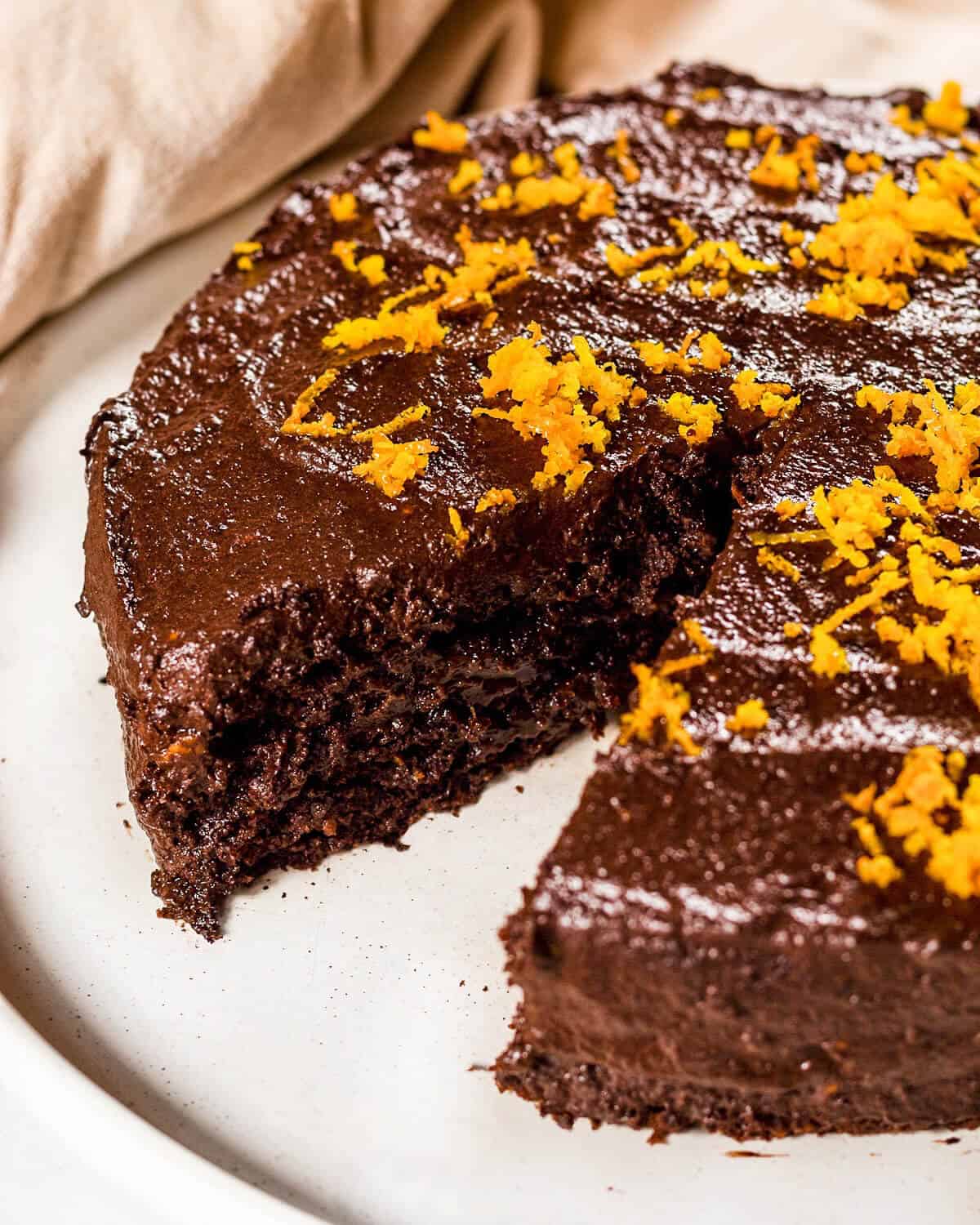 A chocolate orange cake on a white plate, there is a slice missing and you can see the moist texture.