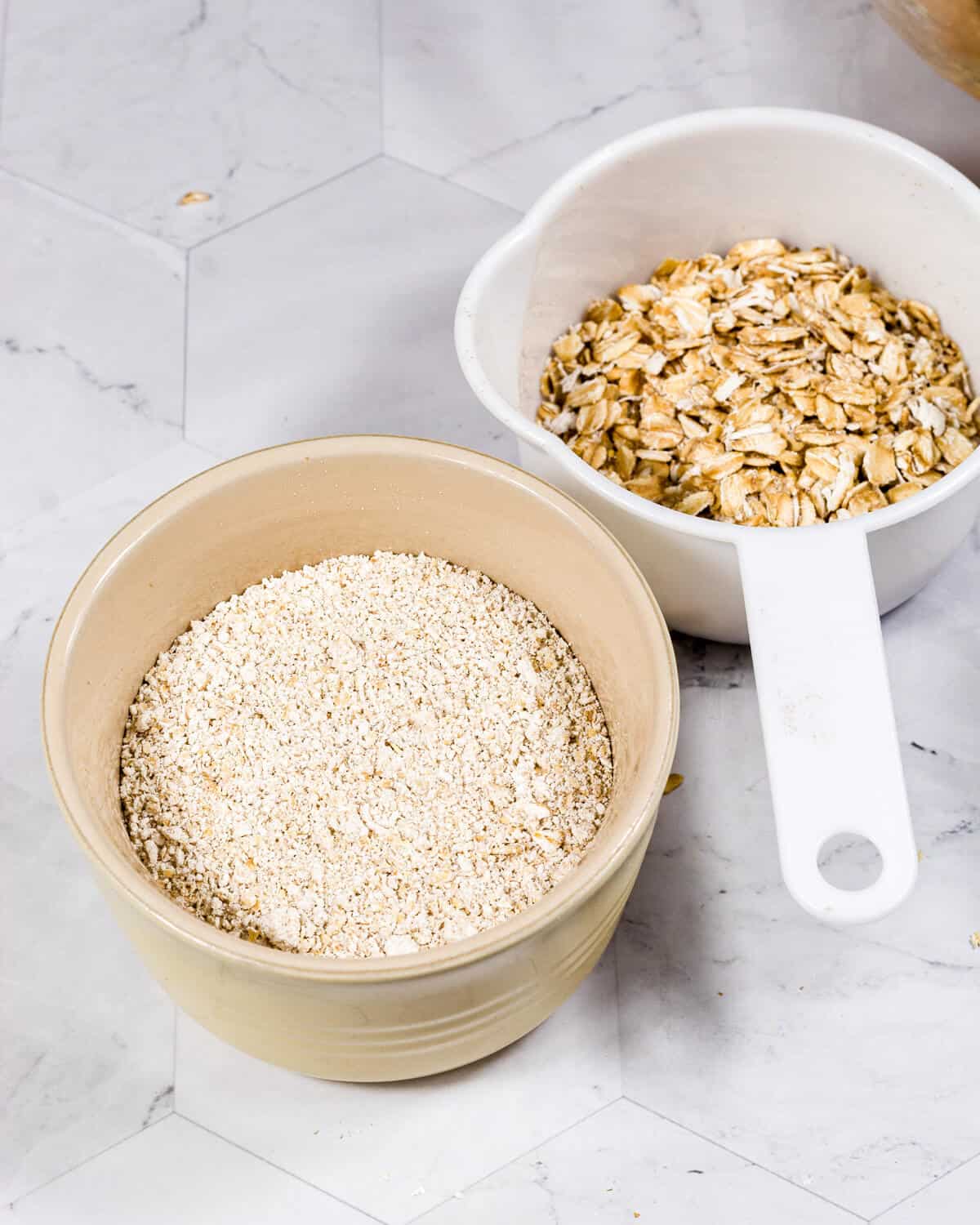 A bowl of blended oats next to a baking cup with rolled oats.
