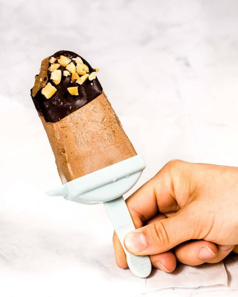 Someone holding a chocolate ice cream bar dipped in chocolate and peanuts. A bite has been taken.