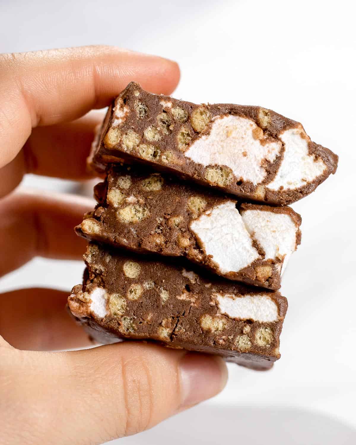 A hand holding three rocky road protein bars.