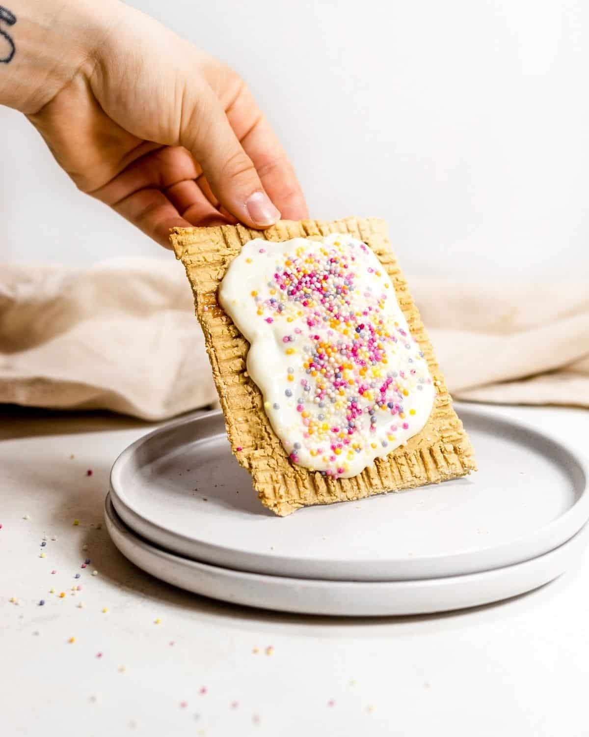 Someone holding a pop tart at an angle on a white plate.