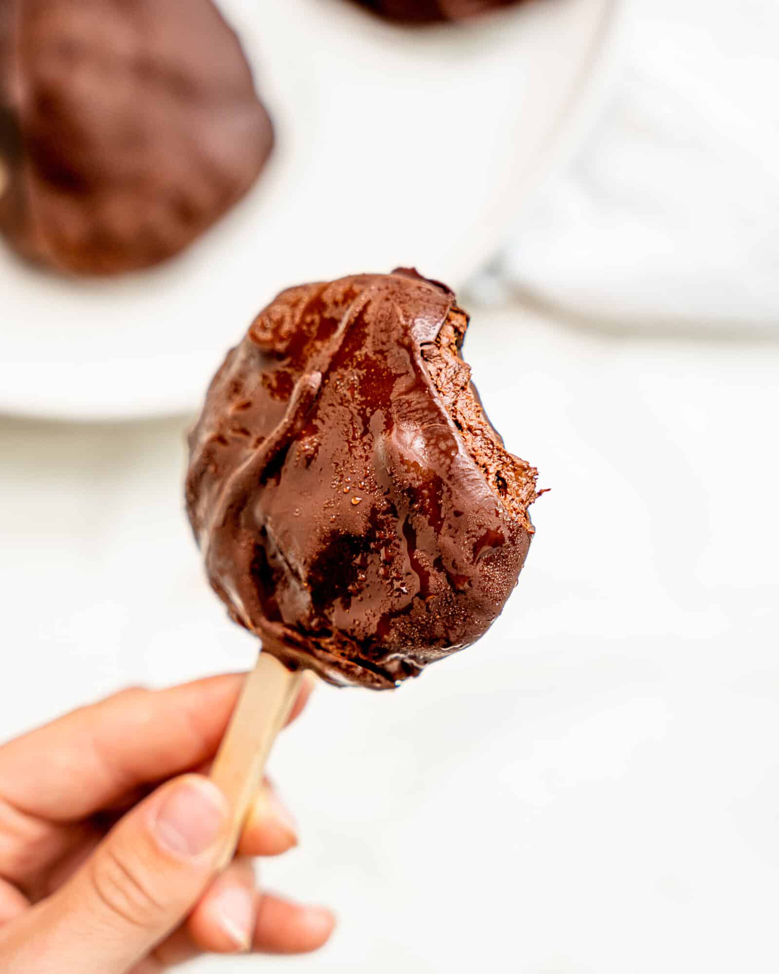 a hand holding a healthy chocolate ice cream bar - a bite has been taken revealing the creamy filling.