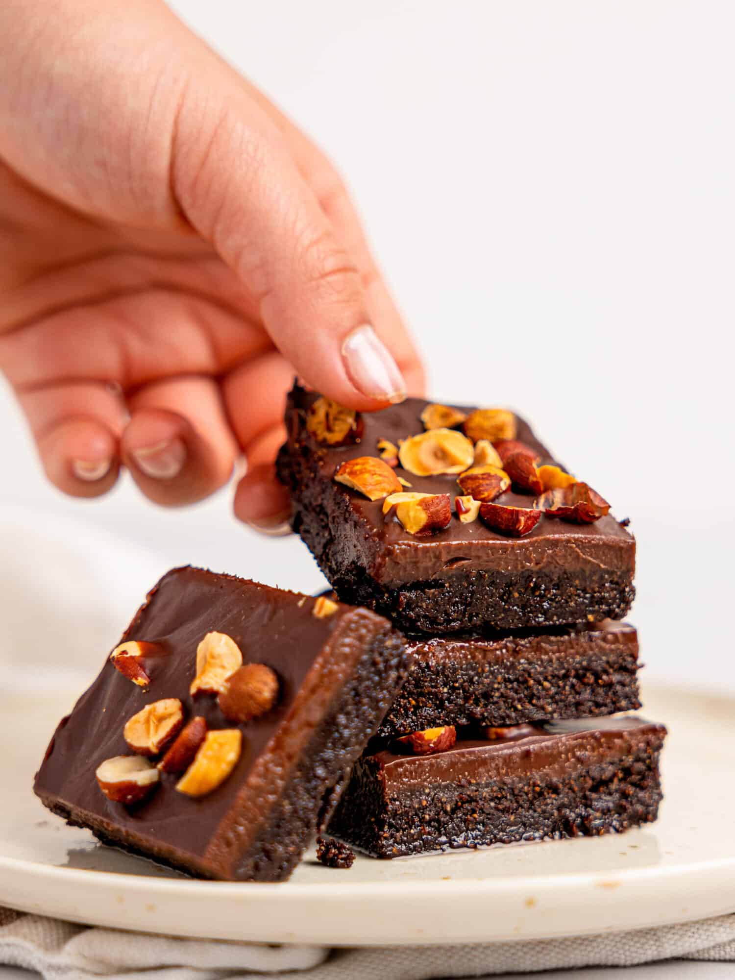 Four No-Bake Brownies stacked on a plate, a handing holding the top brownies.