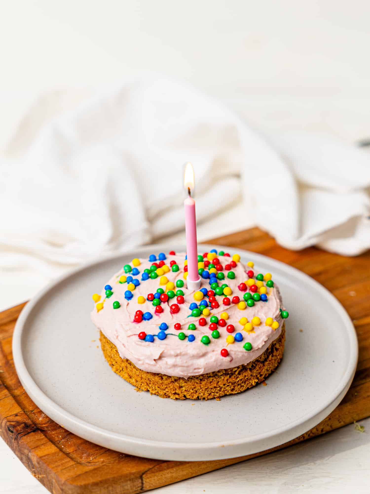 A single-serve birthday with pink protein frosting and sprinkles on a plate. There's a lit candle in the cake.