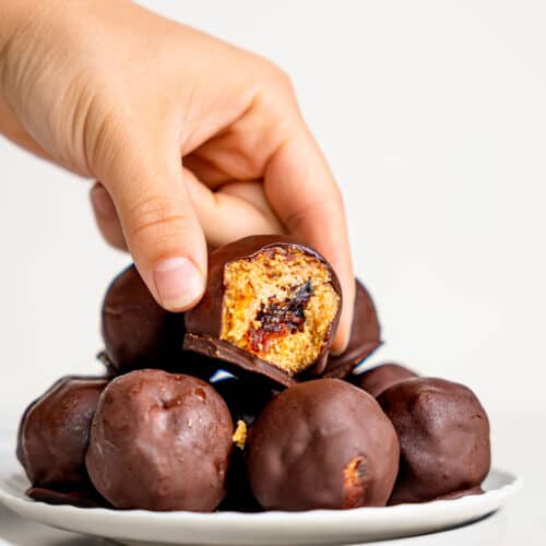 Snickers Energy Balls on a plate. a hand is holding one that a bite is missing from, as if picking it up.