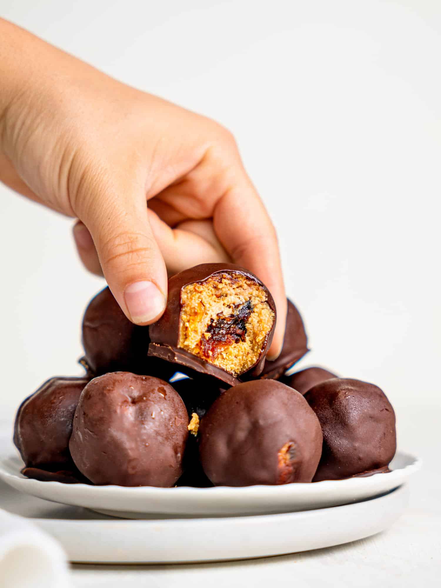 Snickers Energy Balls on a plate. a hand is holding one that a bite is missing from, as if picking it up.