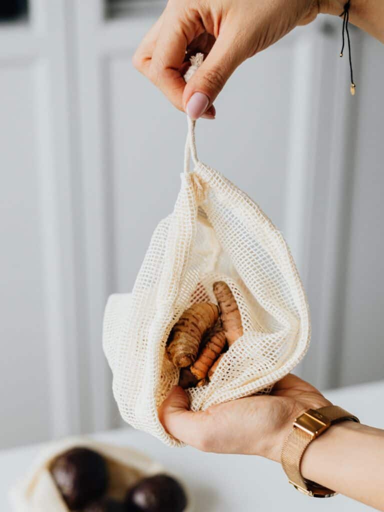 Fresh turmeric in a cheesecloth bag. someone is holding the bag revealing the contents.