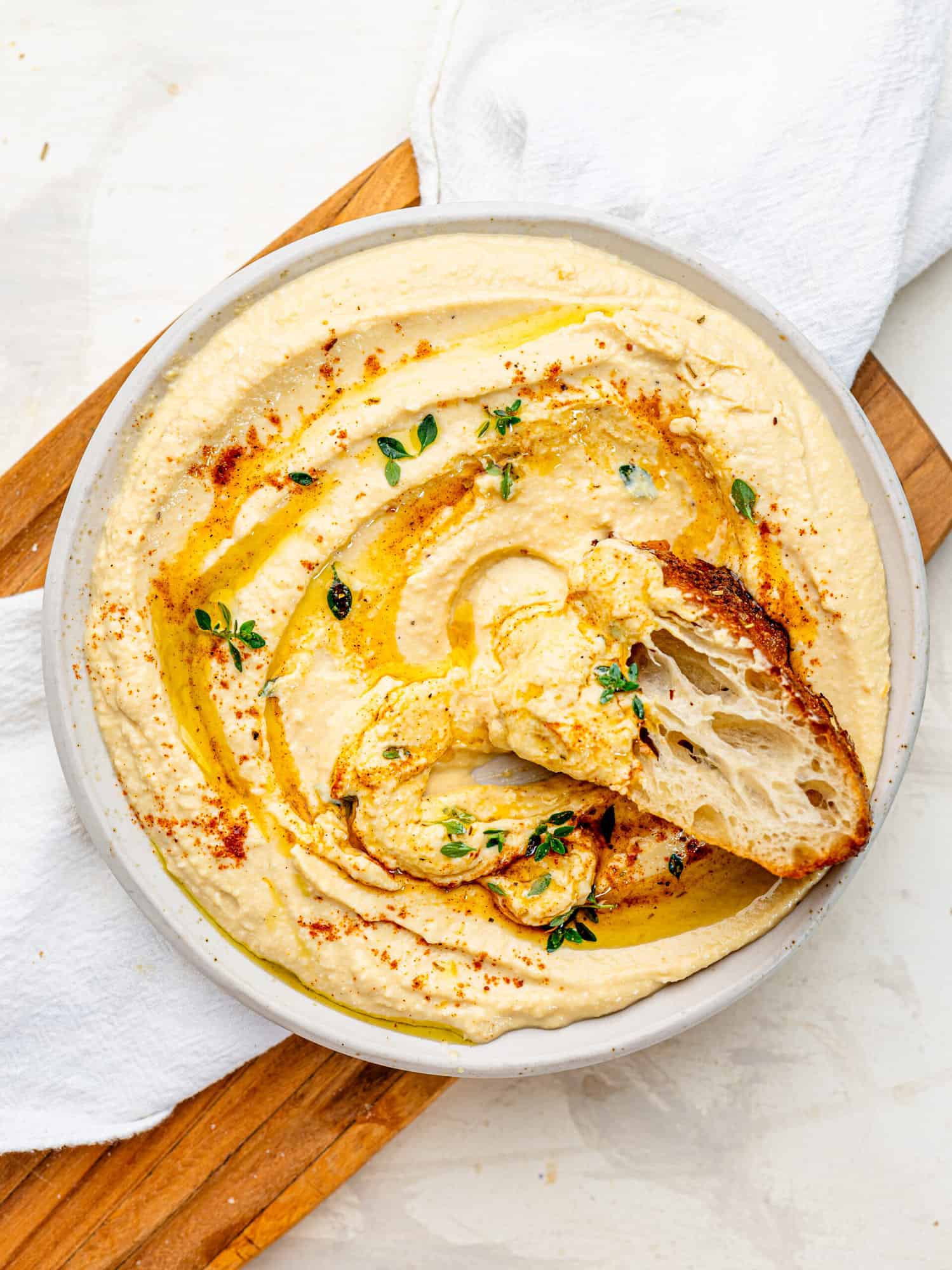 Creamy Cottage Cheese Hummus with a drizzle of olive oil spread out on a plate. There is a piece of foccaccia dipped into the hummus.