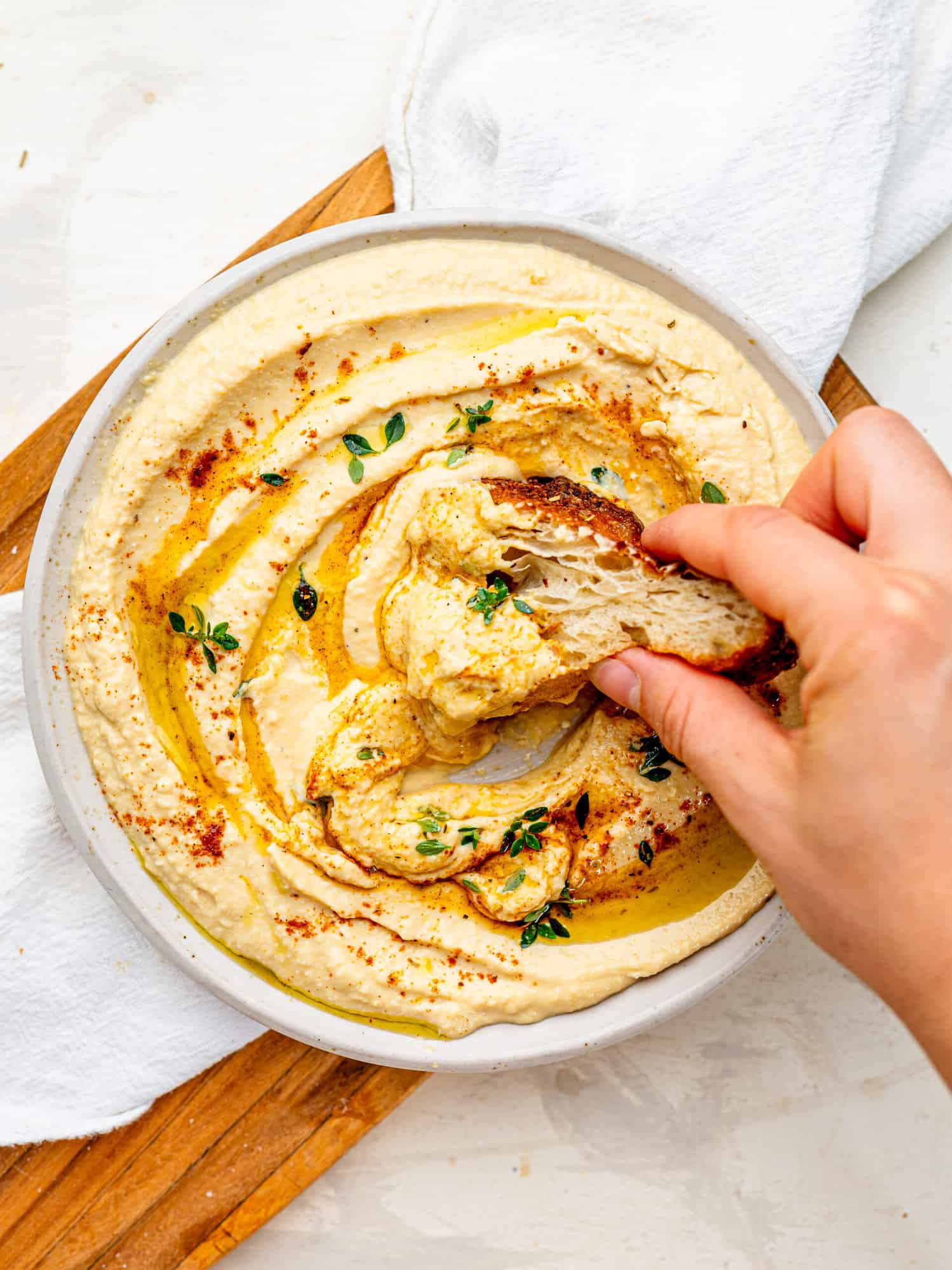 Creamy Cottage Cheese Hummus with a drizzle of olive oil spread out on a plate. Someone is dipping a piece of focaccia in it.