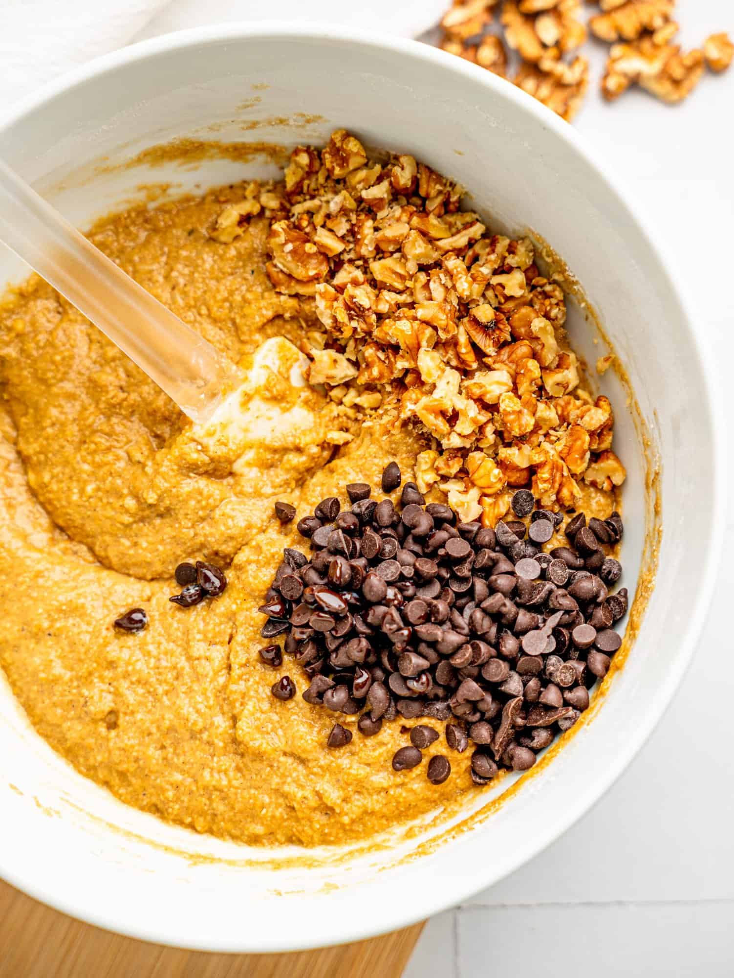 healthy oat flour banana bread ingredients combined in a bowl with chocolate chips and walnuts.