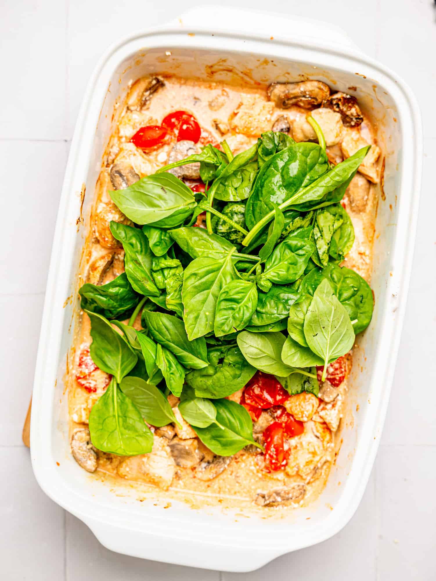 Adding spinach and basil to the baked chicken and feta.
