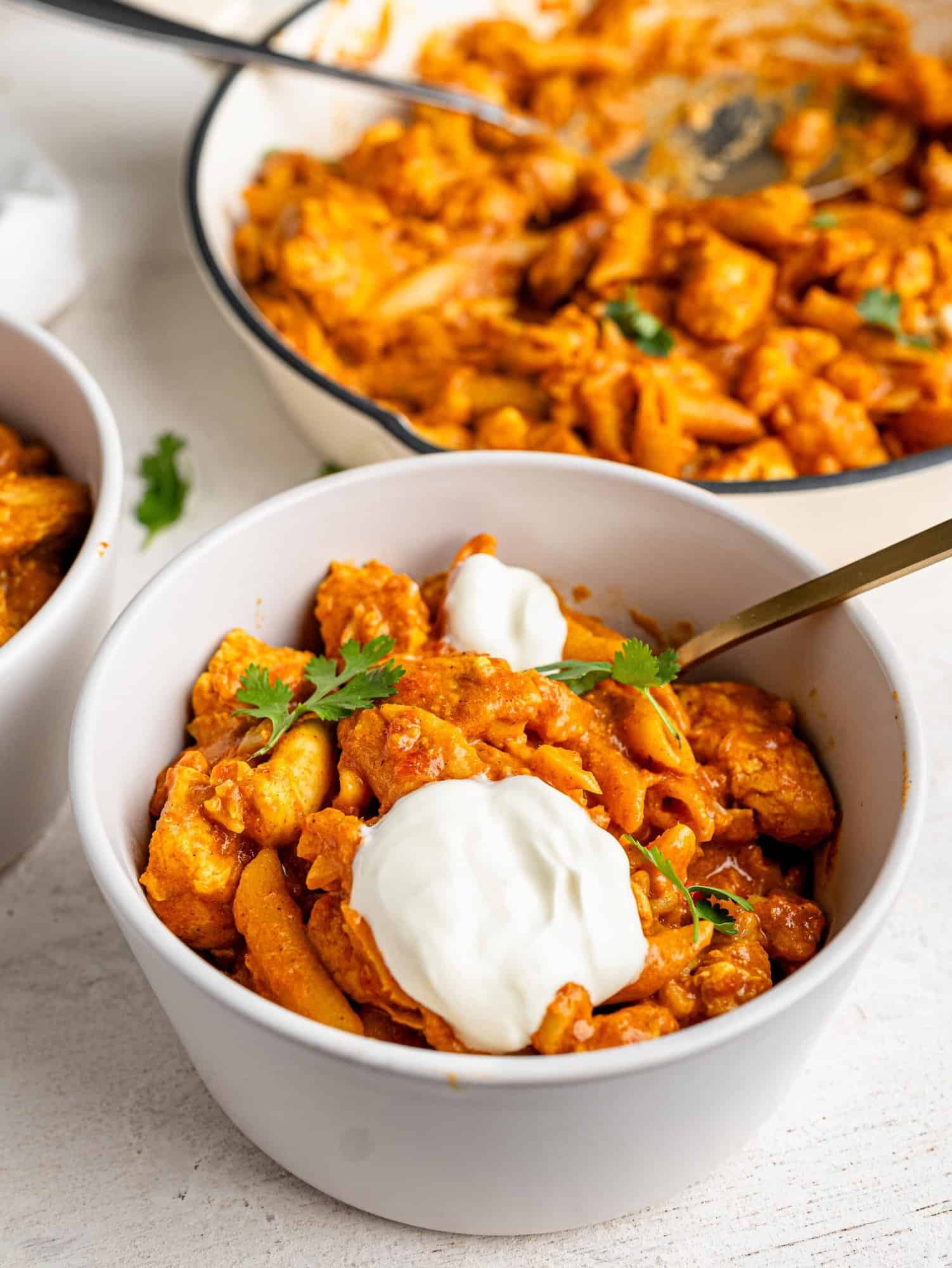 Butter Chicken Pasta in a white bowl topped with cilantro and yogurt.