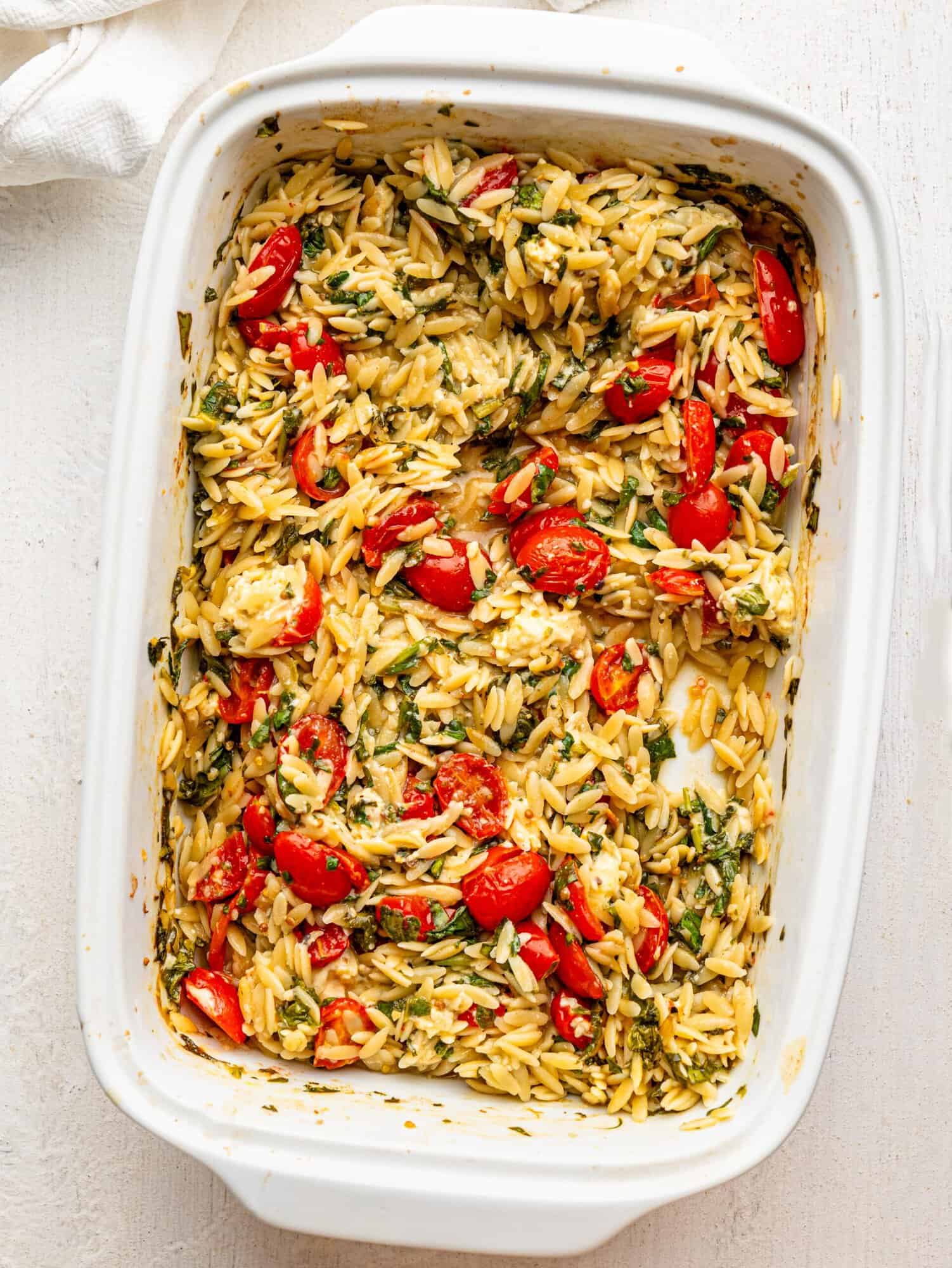 Orzo with feta, spinach and tomatoes in a white casserole dish.
