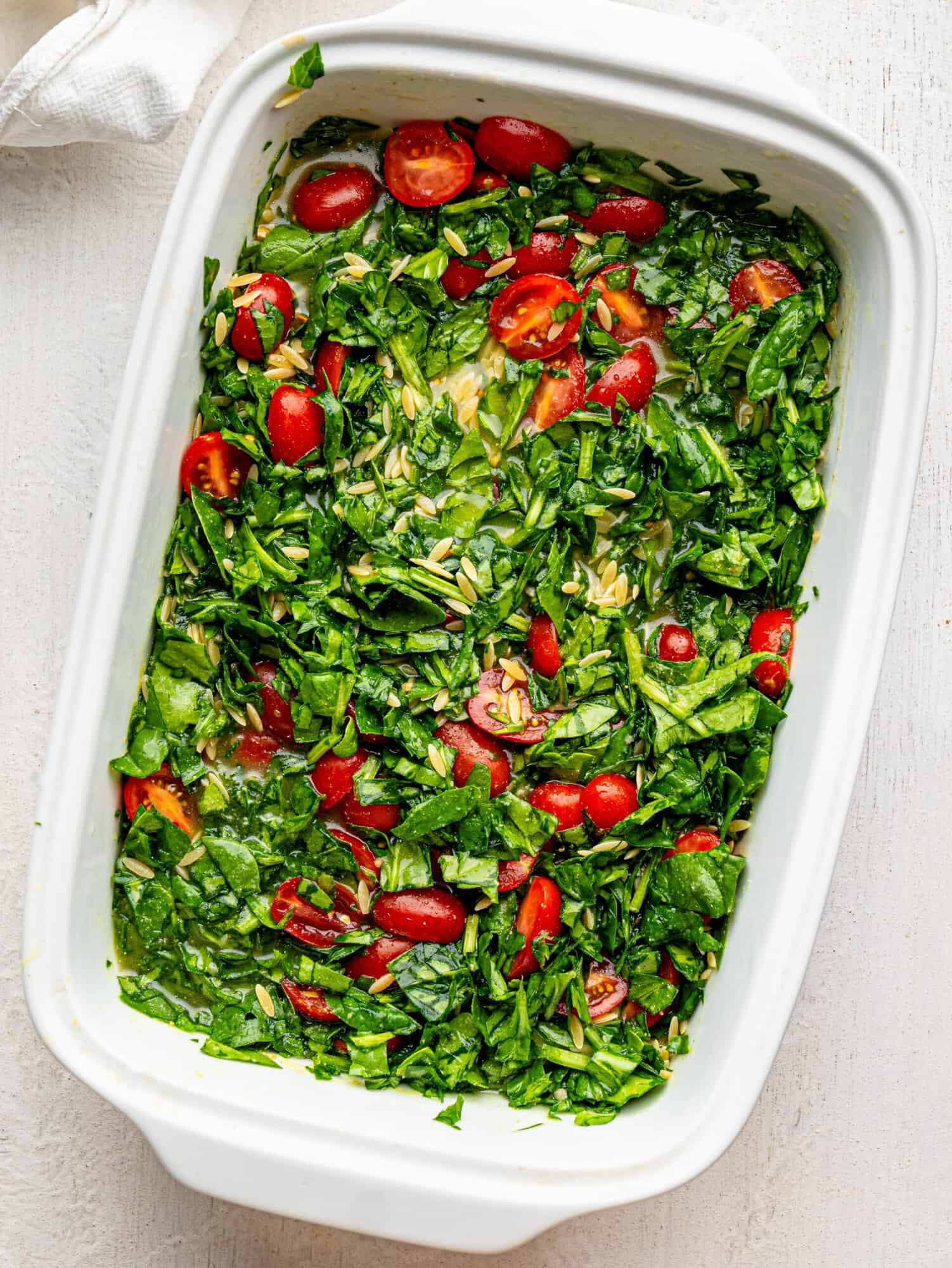 Orzo with feta, spinach and tomatoes in a white casserole dish before baking.