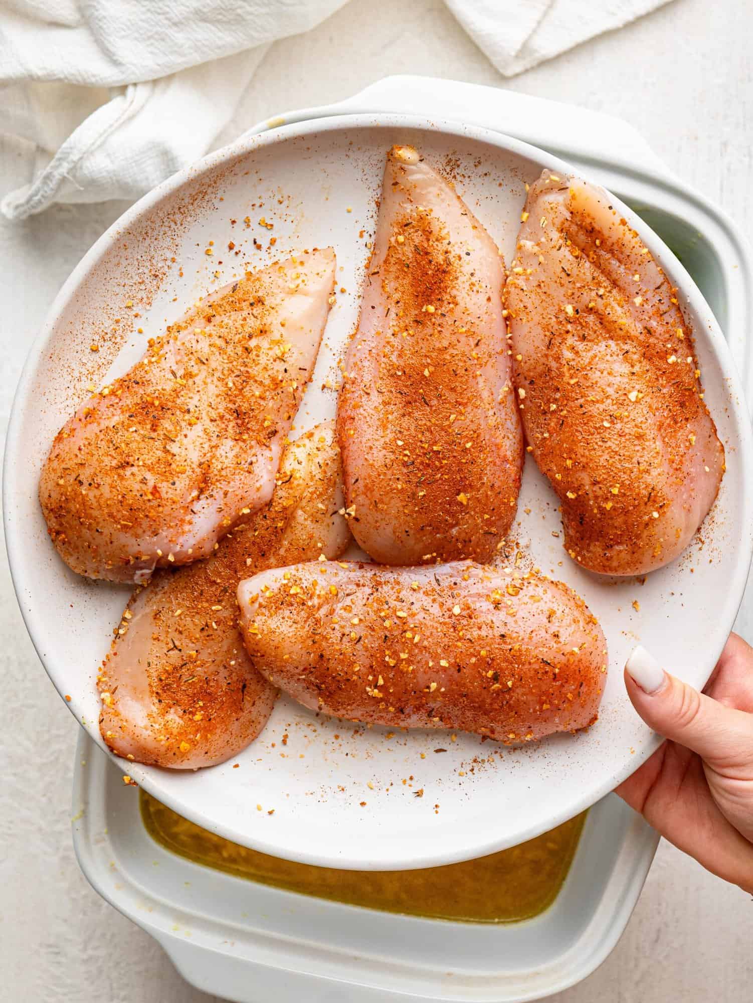 Seasoned raw chicken breasts on a white plate.