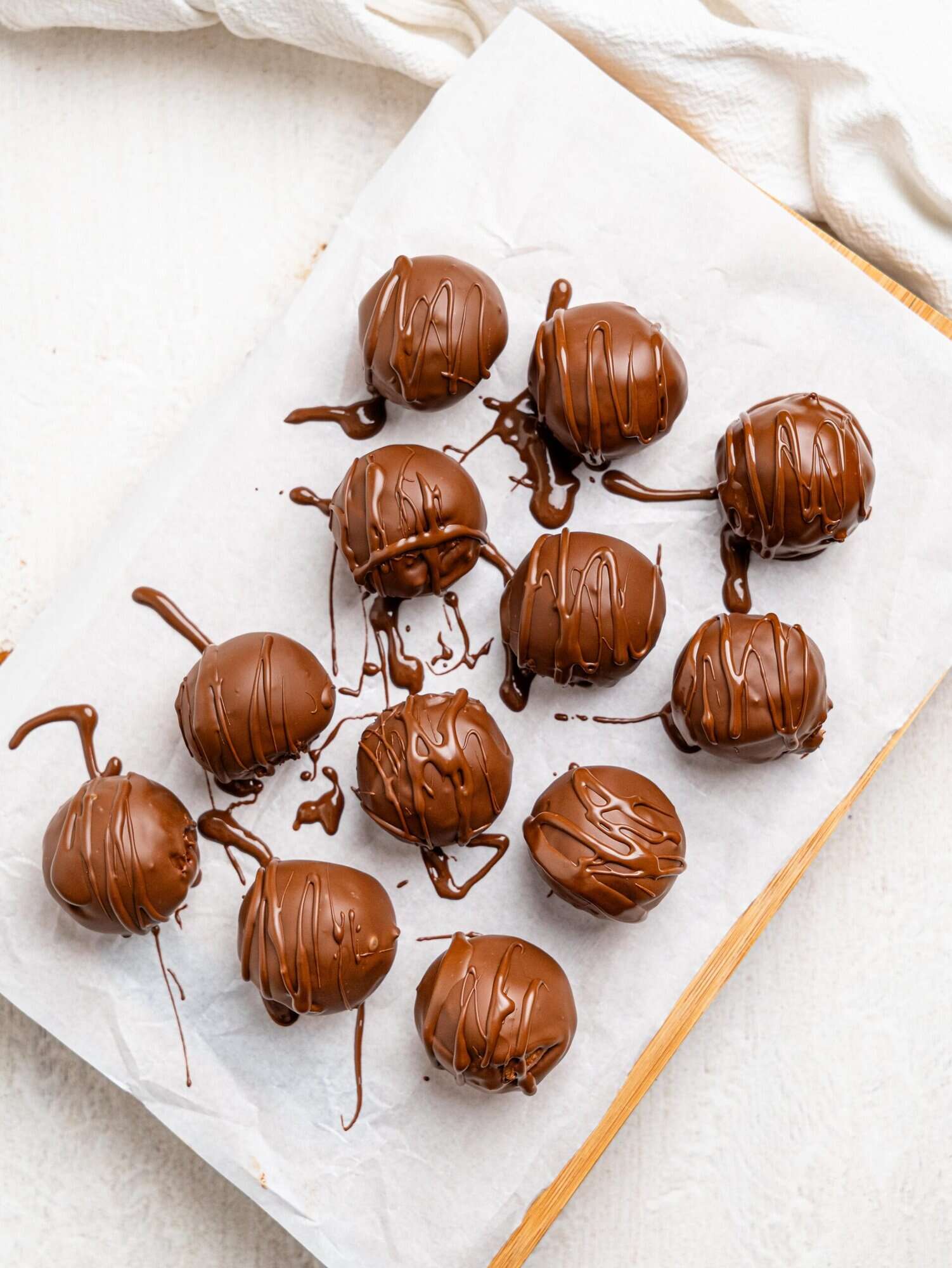 Healthy cookie dough balls dipped in dark chocolate on a sheet of parchment paper.