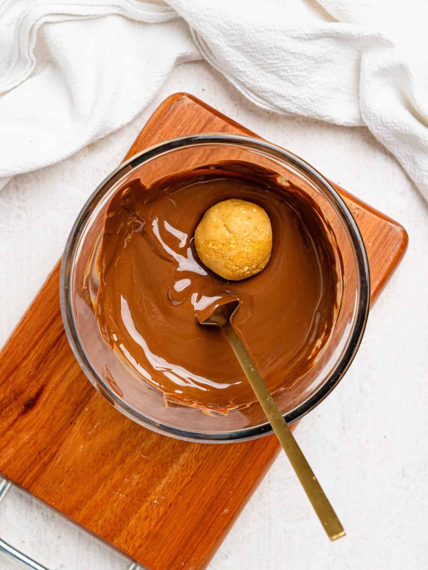 Healthy chickpea cookie dough balls being dipped in dark chocolate.