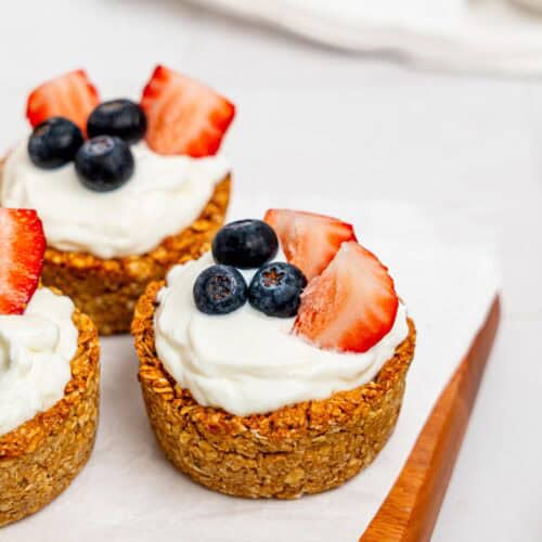 Granola Cups filled with yoghurt and berries on a wooden board.
