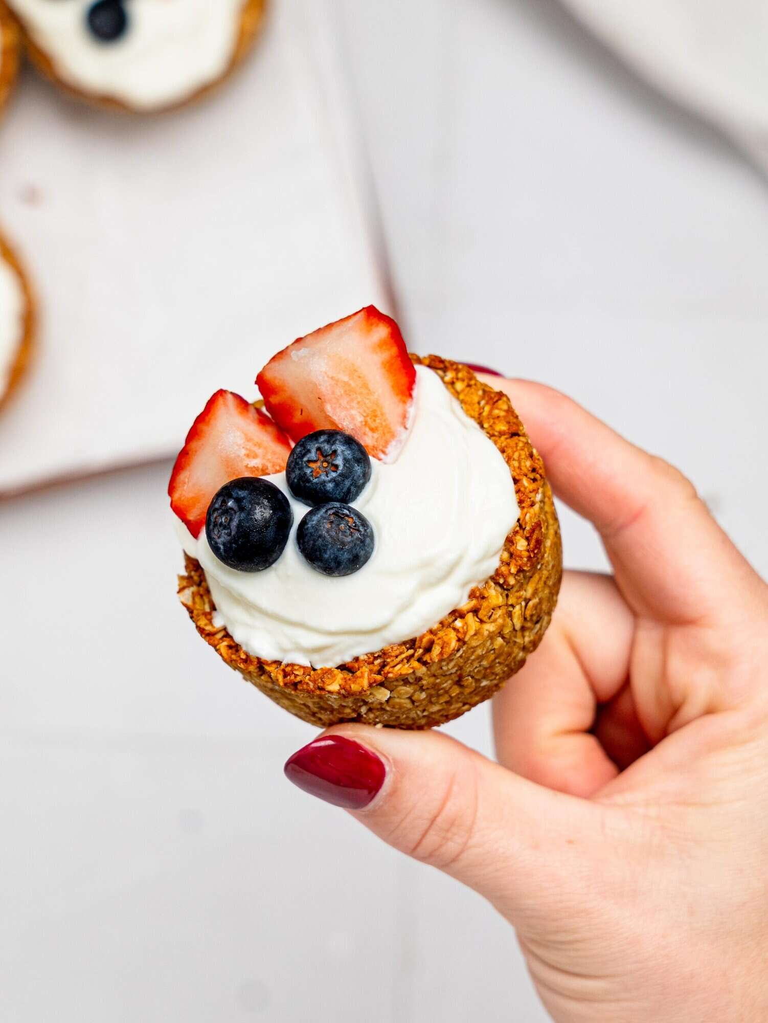A hand holding a granola cup filled with yoghurt and berries.