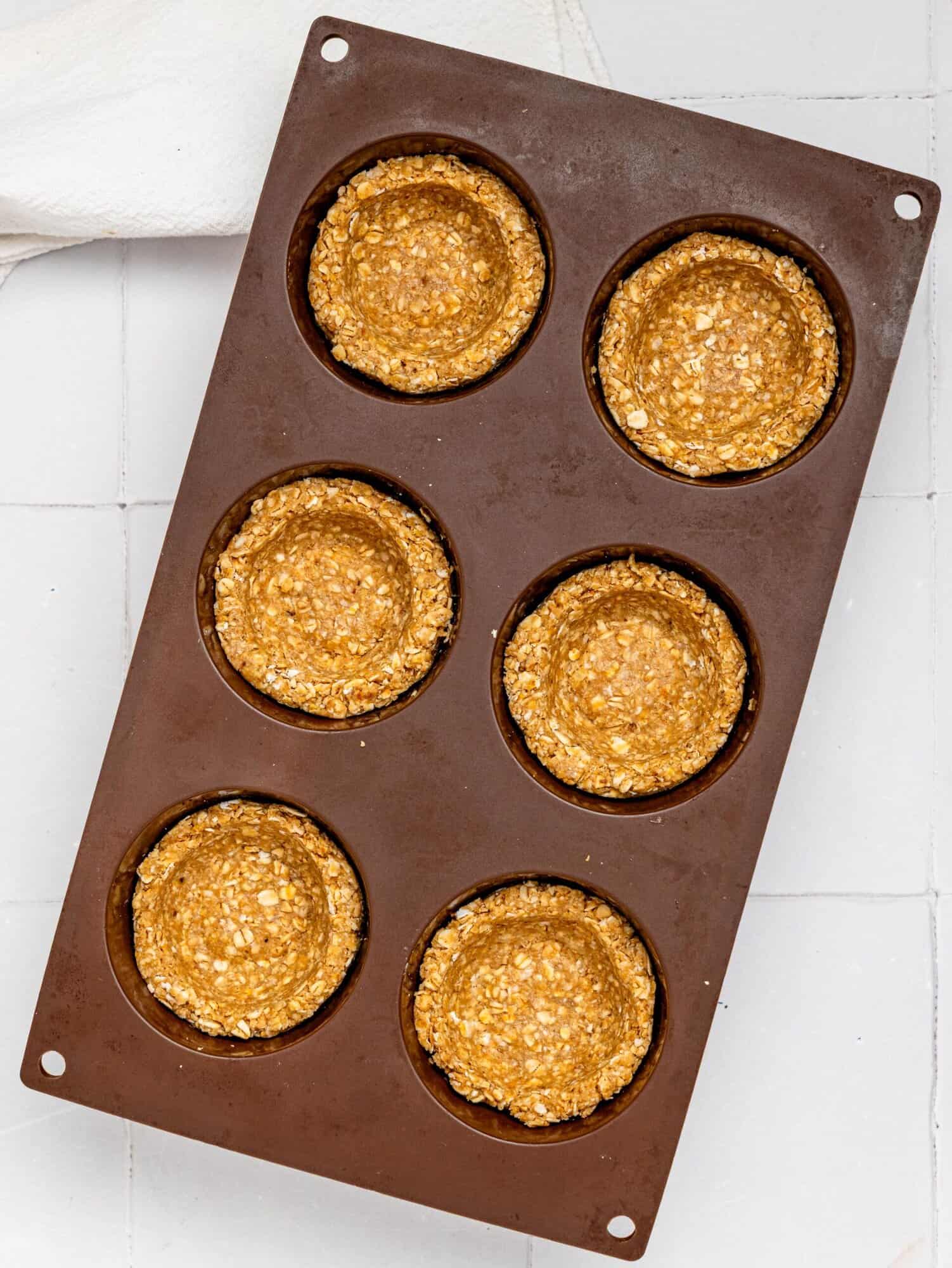 Granola cup mixture pressed in a silicone muffin tray.