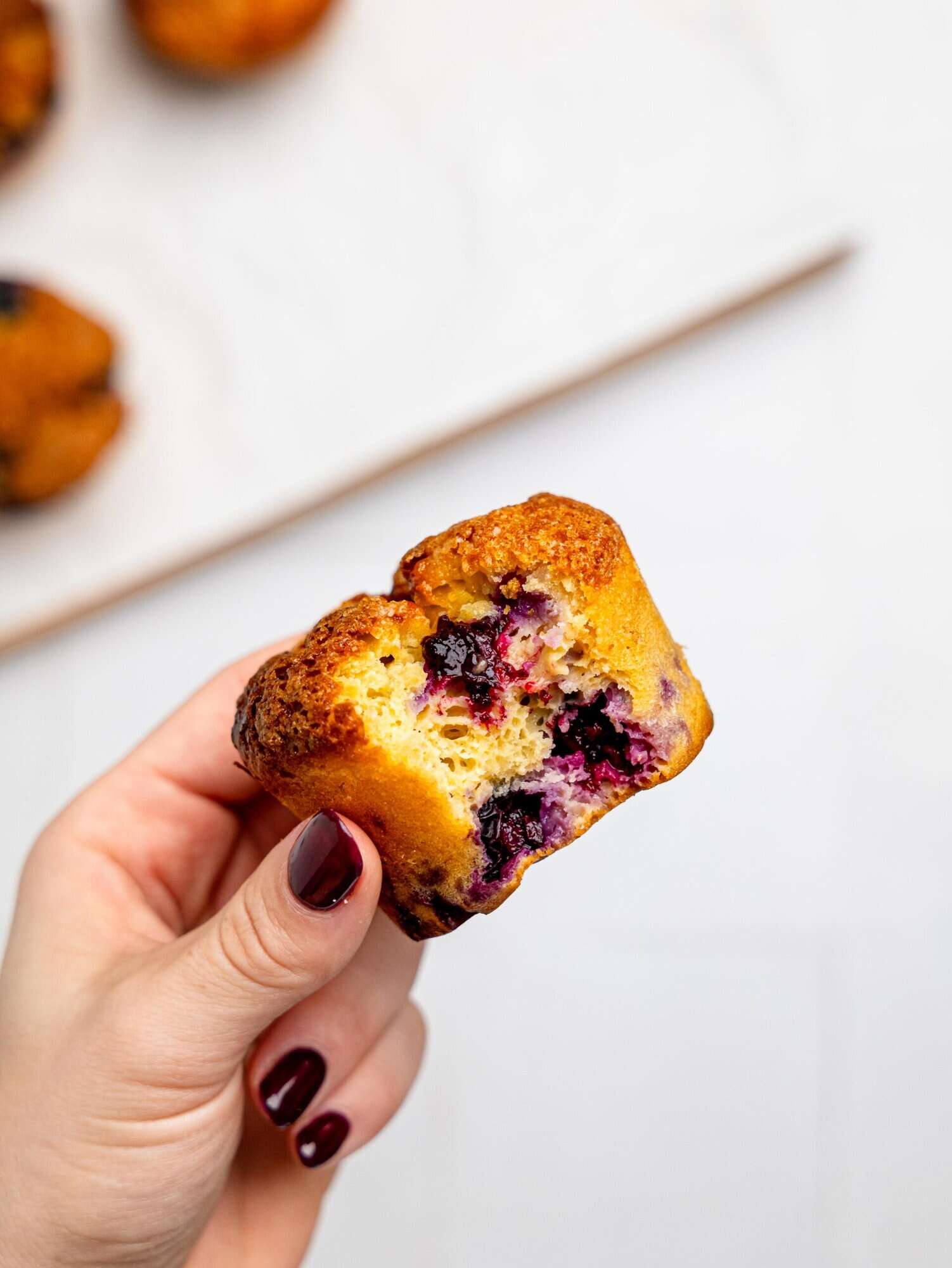 A hand holding a half-eaten blueberry cottage cheese muffin.