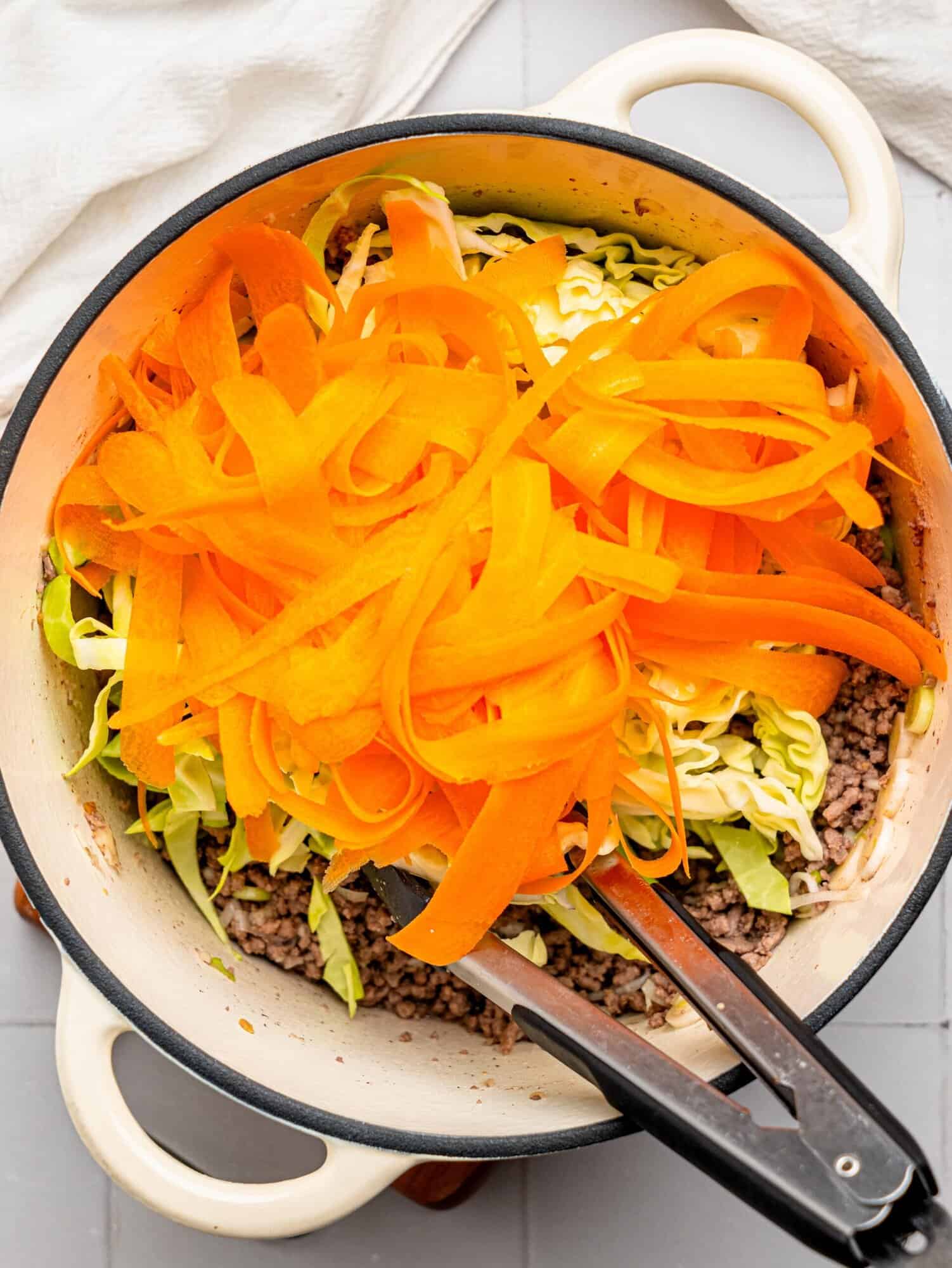 Lean beef mince, ginger, garlic, spring onion, carrots, and cabbage in a large pot.