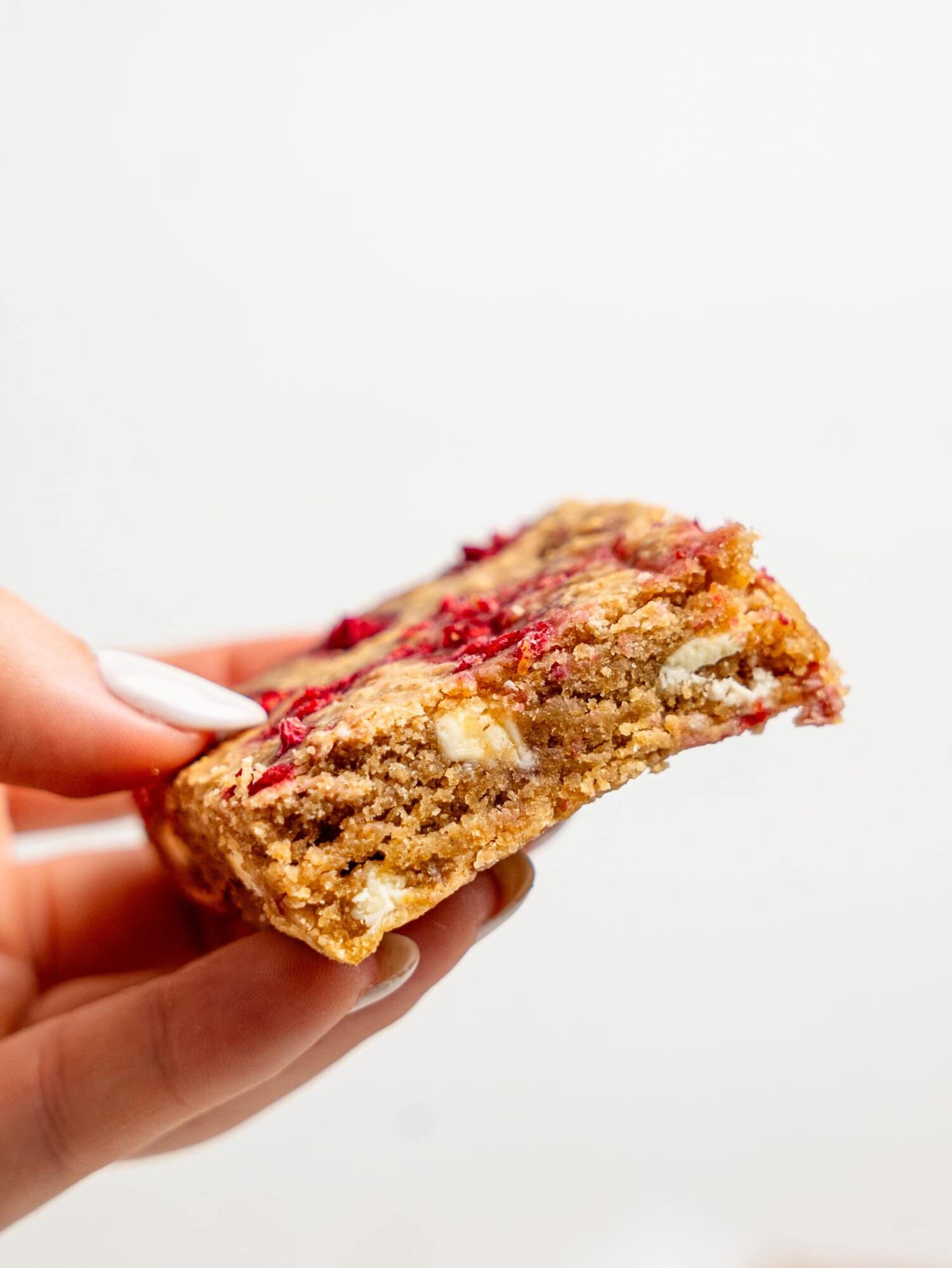 A hand holding aRaspberry and White Chocolate Blondie.