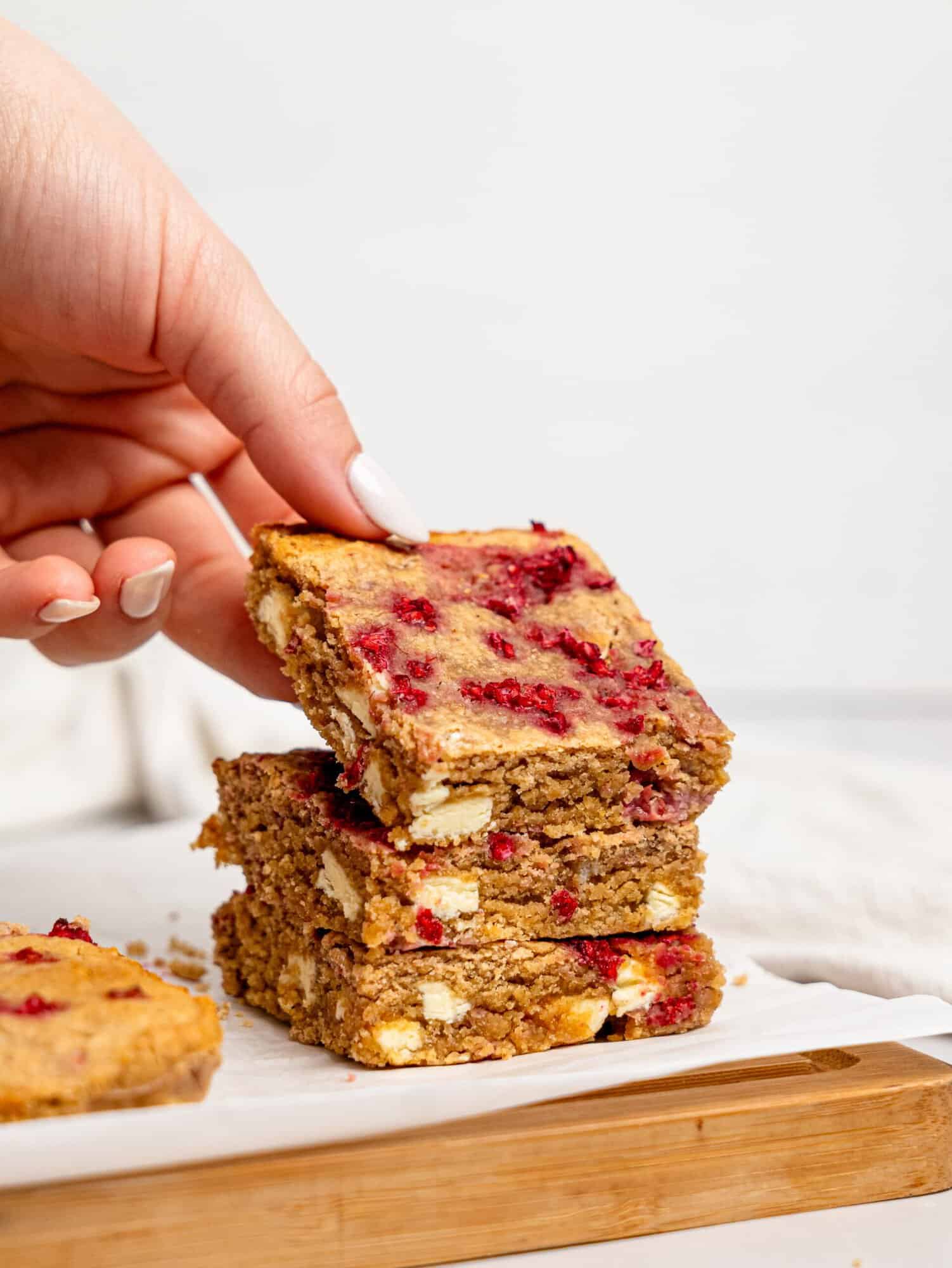 Three Raspberry and White Chocolate Blondies on a chopping board.