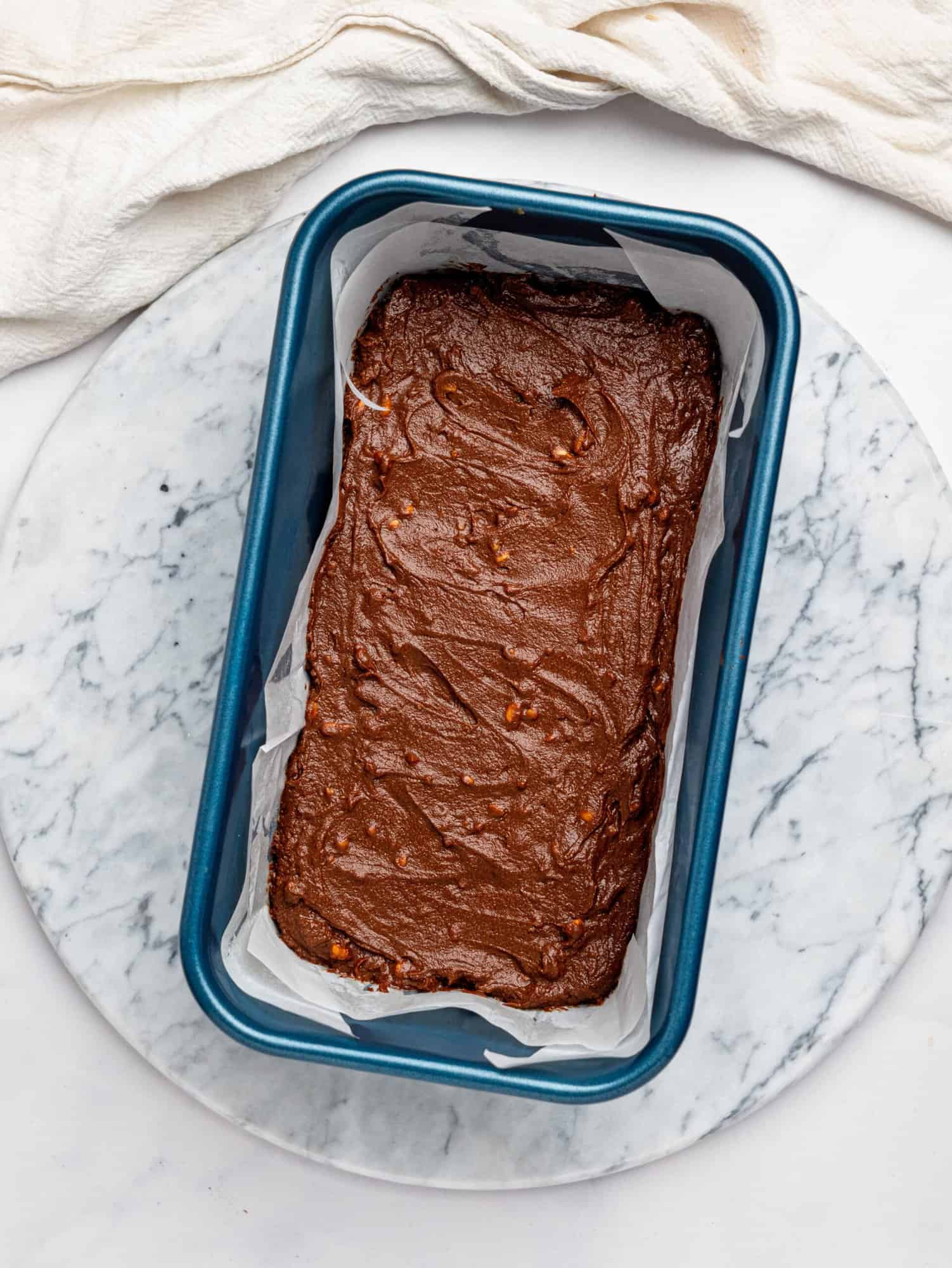 3 ingredient fudge mixture pressed in a blue loaf pan lined with parchment paper.