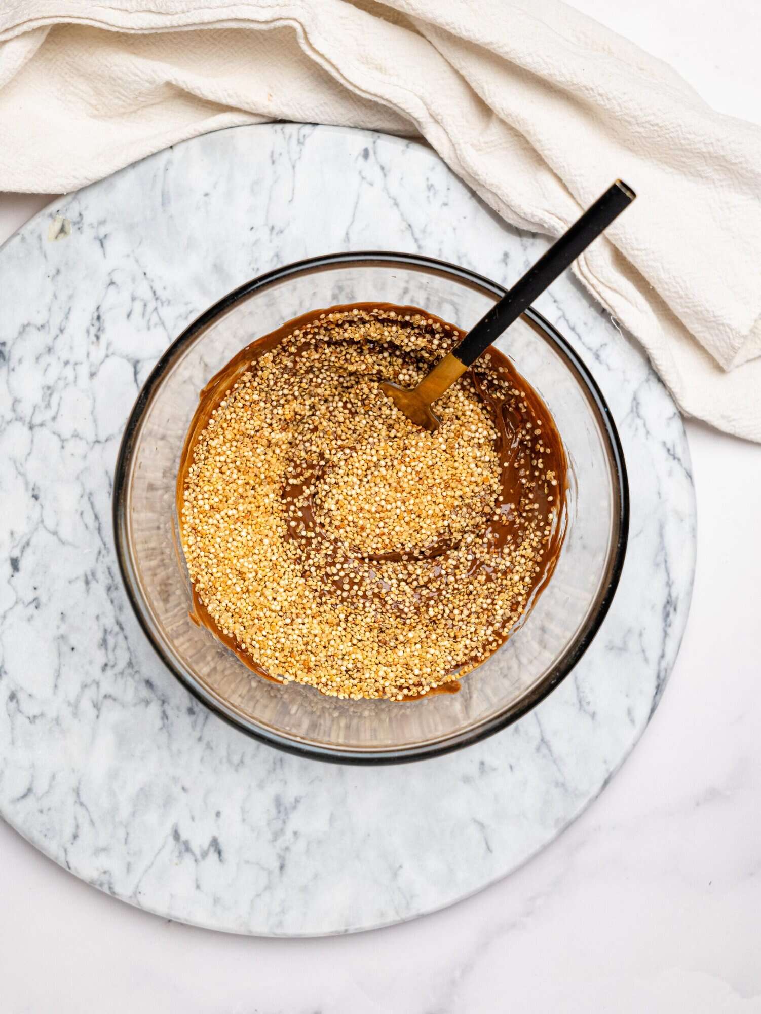 Melted dark chocolate and peanut butter, with toasted quinoa in a glass bowl.