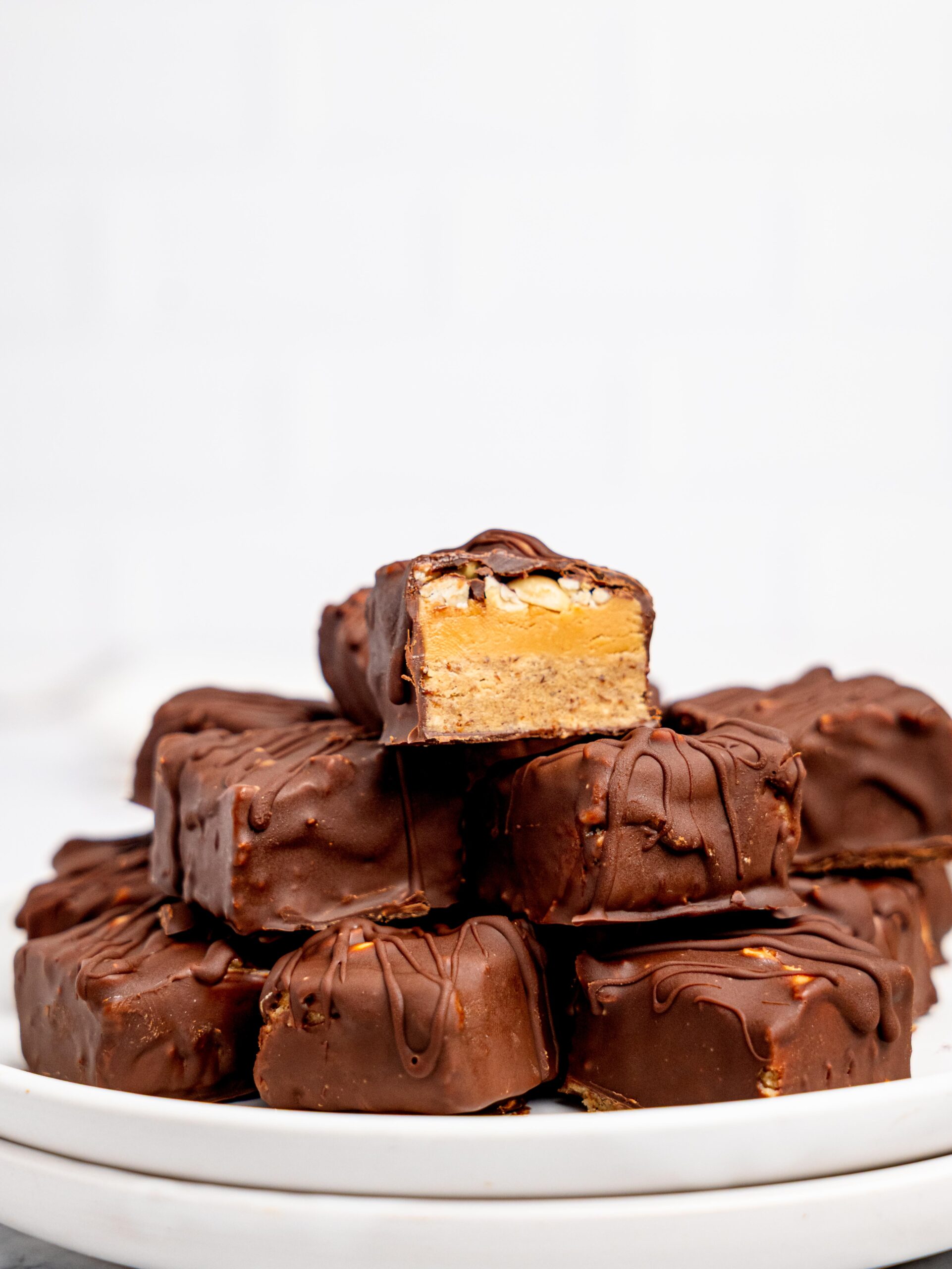 Protein Snickers Bites stacked on a white plate.