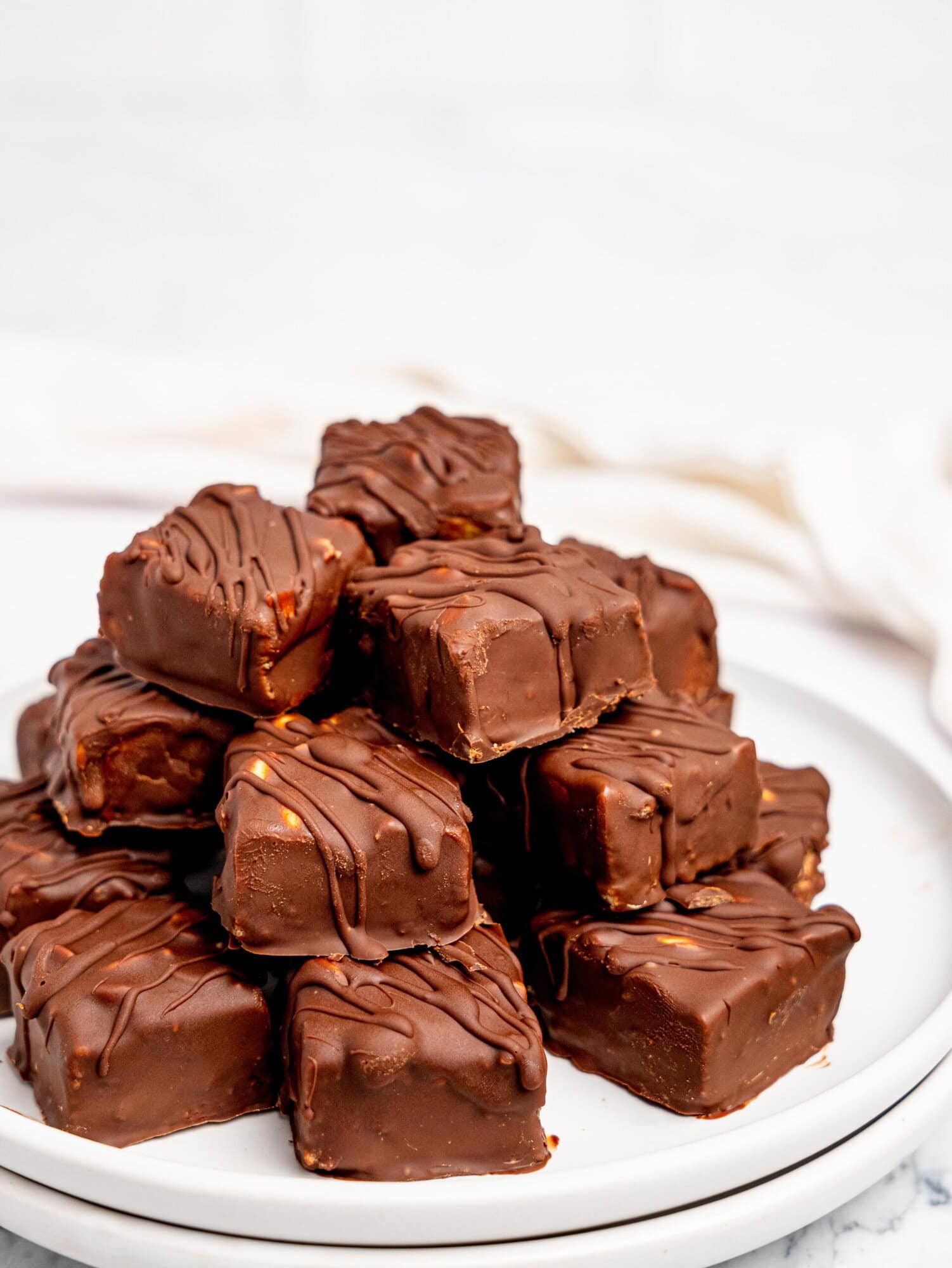Healthy Snickers Bites stacked on a white plate.