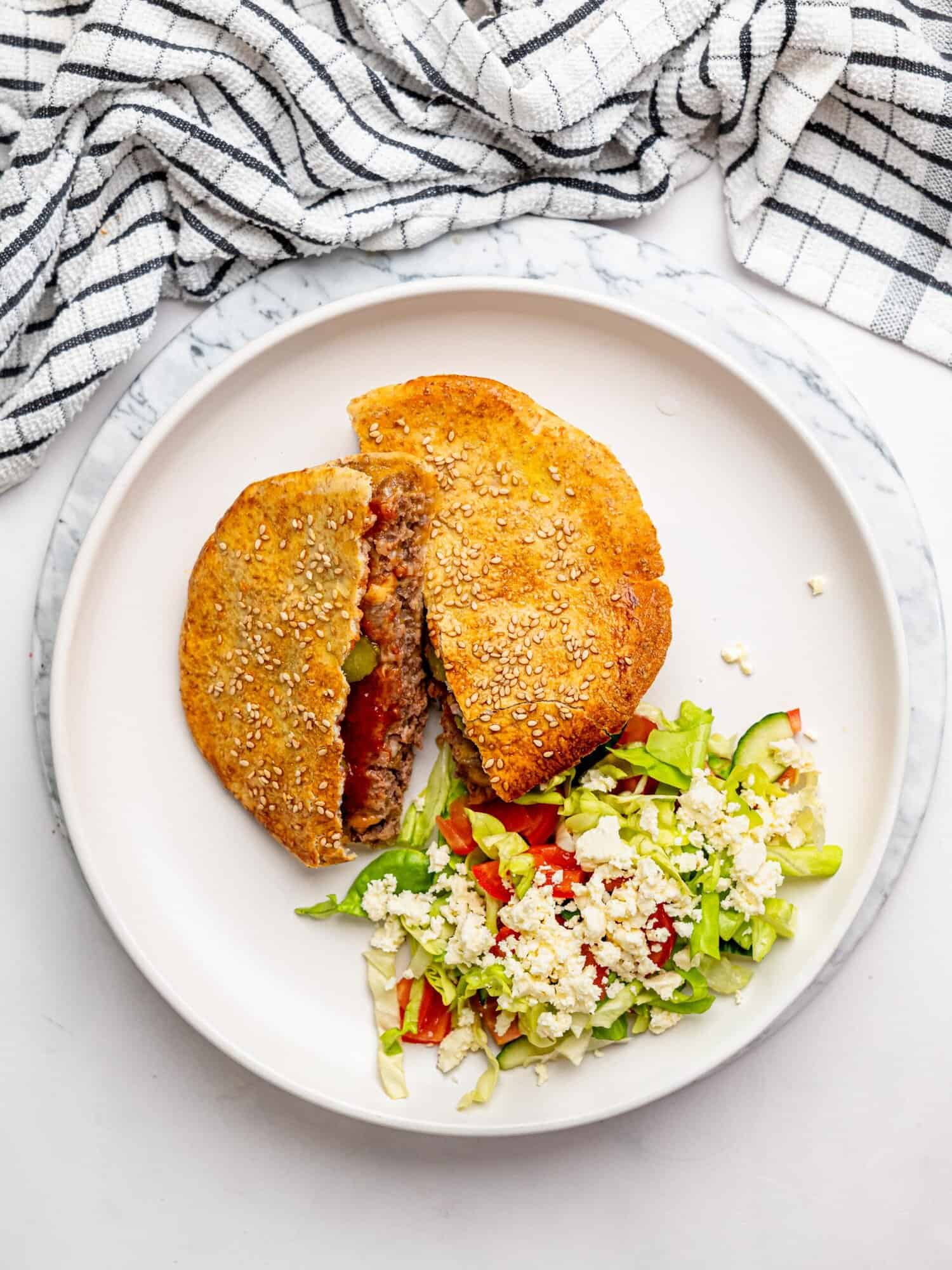 A crispy pita smash burger sliced in half, on a plate, served with a side salad.