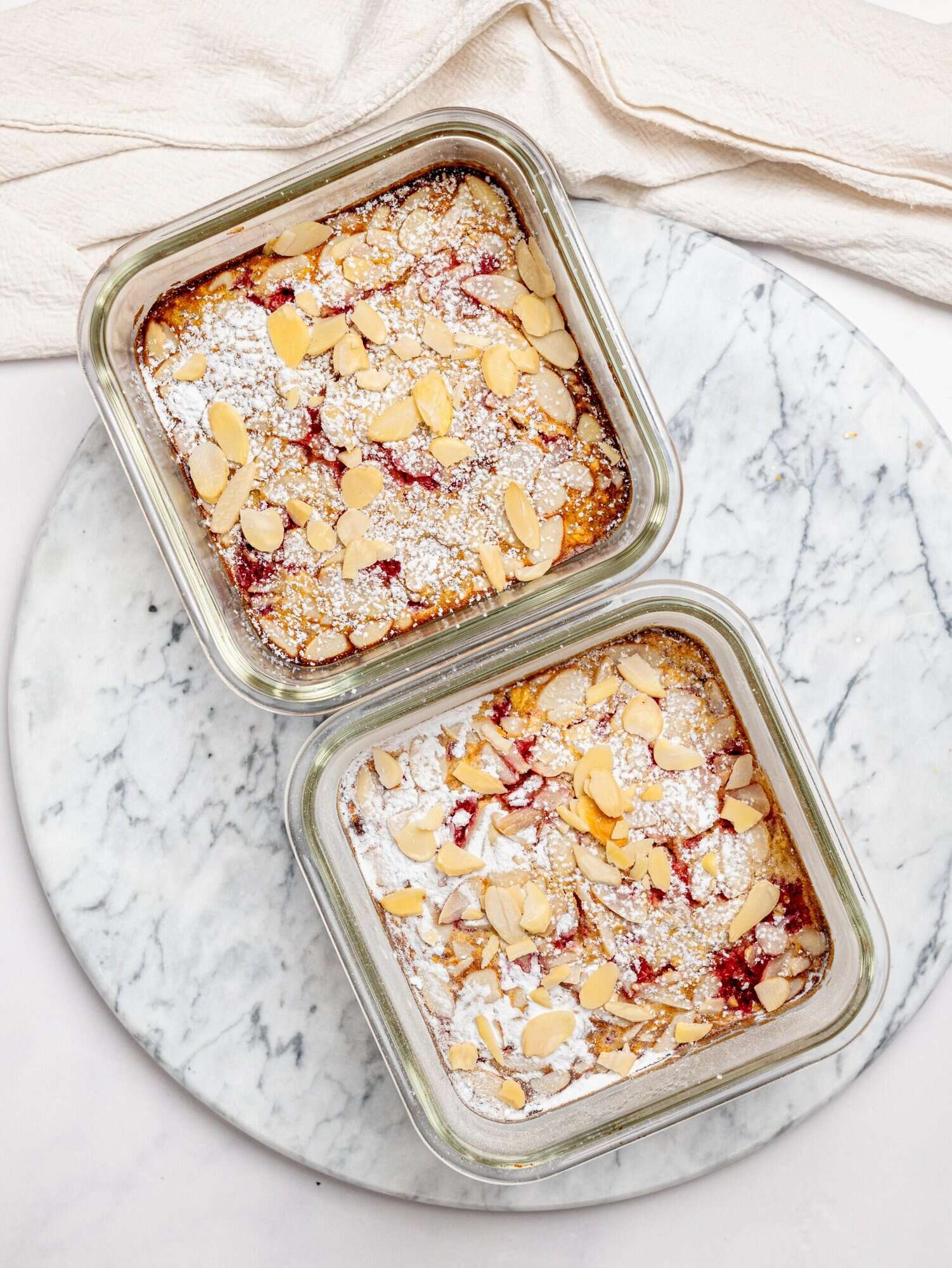 Two servings of raspberry and almond protein baked oats in glass meal-prep containers.