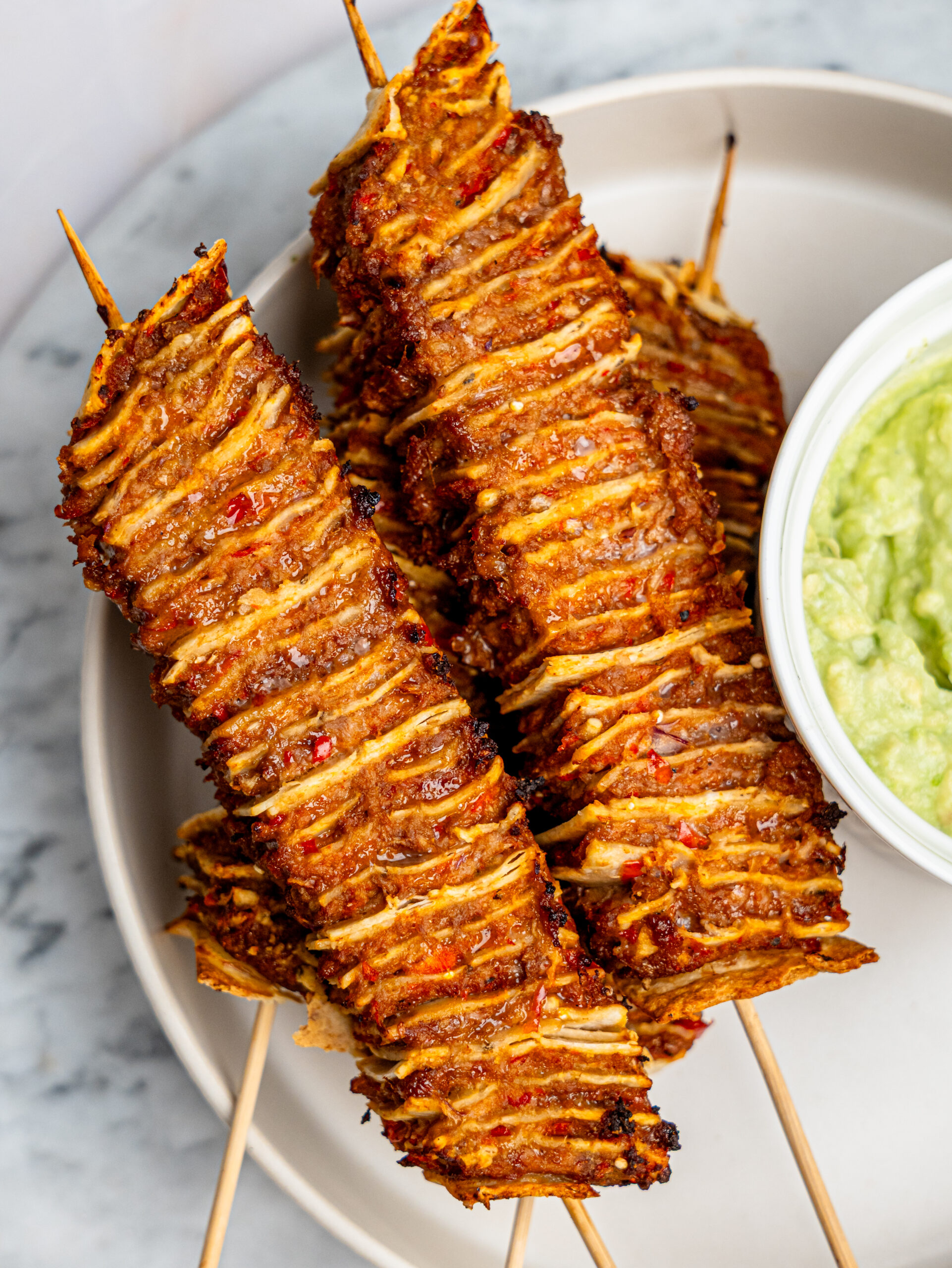 Four tortilla kebab skewers on a plate with a bowl of guacamole.