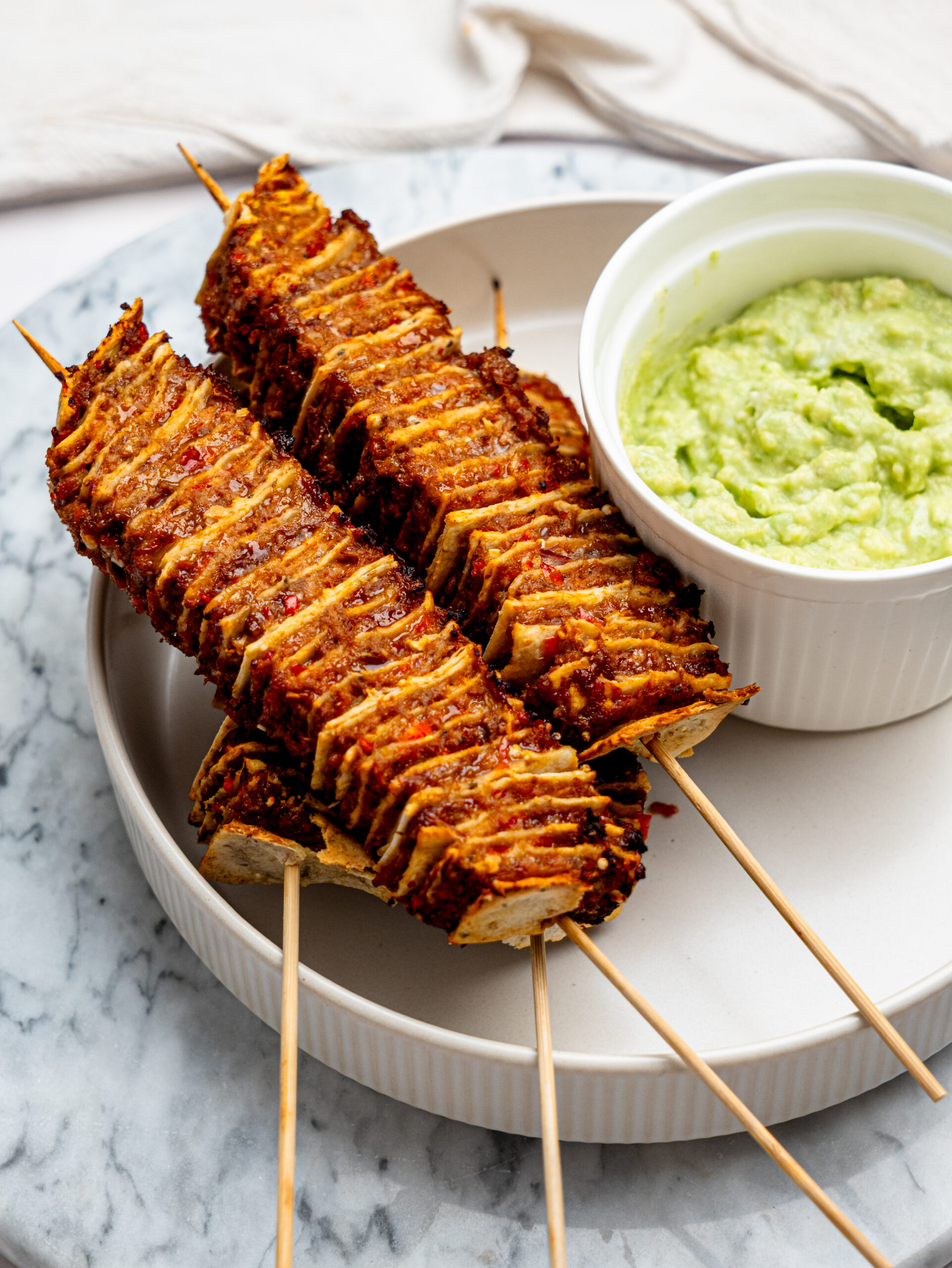 Four tortilla kebab skewers on a plate with a bowl of guacamole.